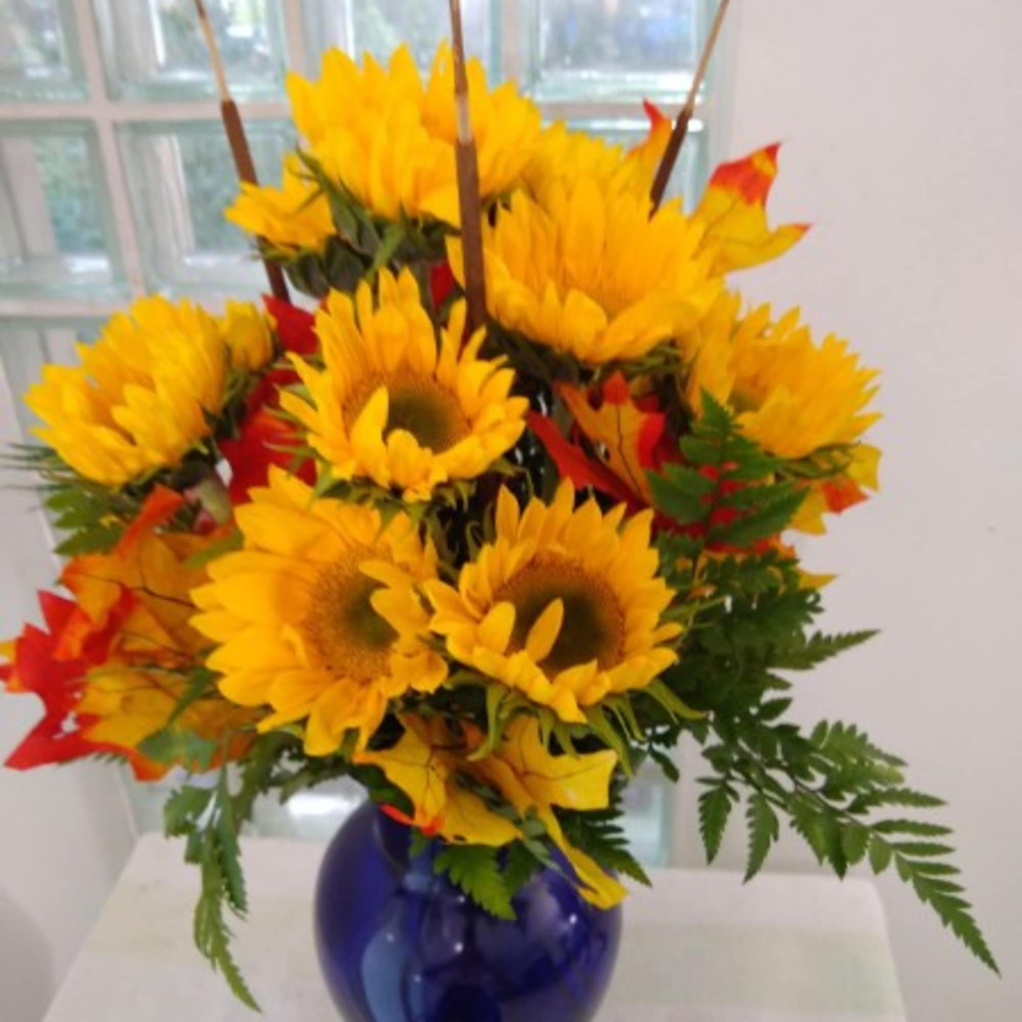 Sunflower arrangement in a blue glass vase with autumn leaves