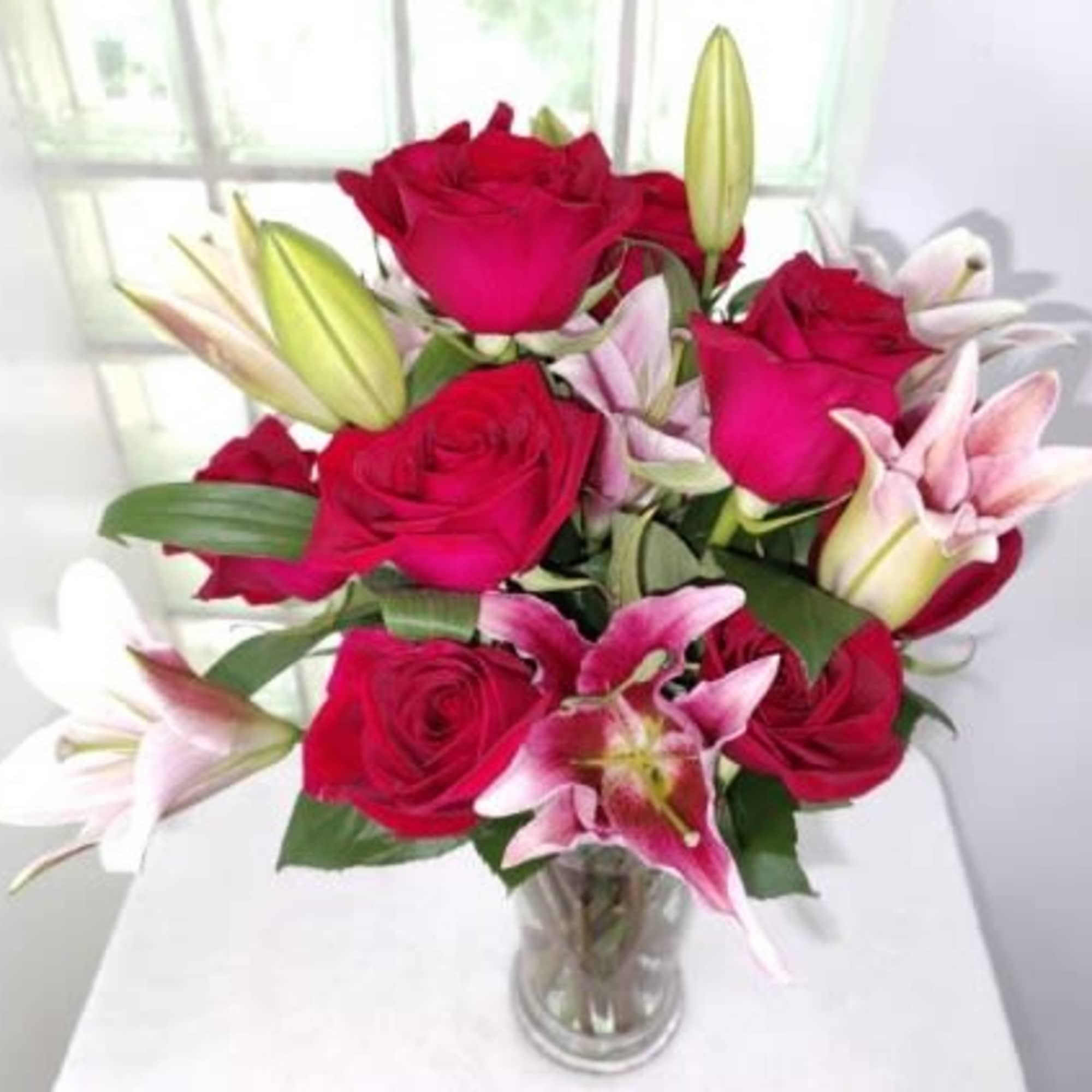 Bouquet of red roses and pink lilies in a clear glass vase