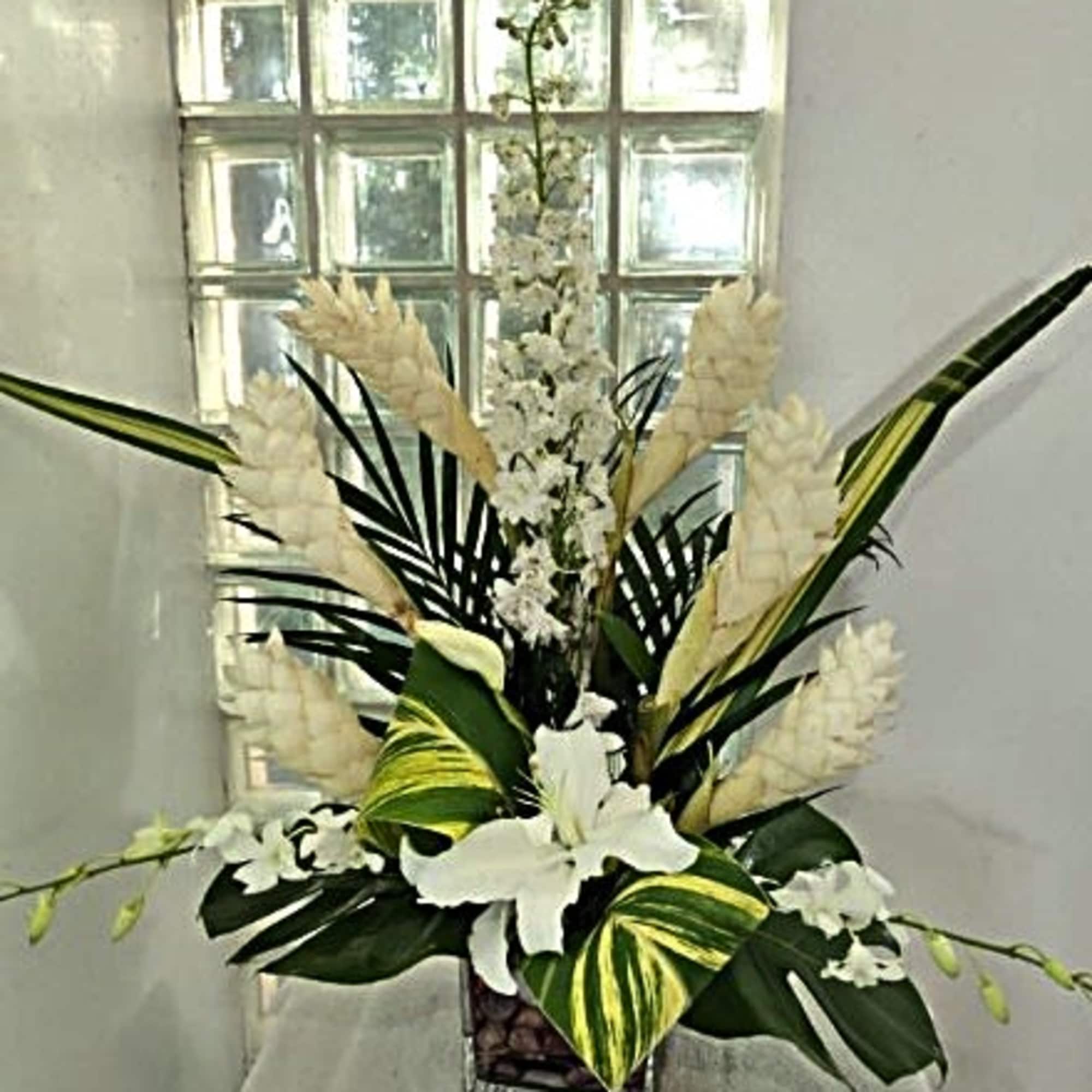 Tall white floral arrangement in a square vase with large tropical leaves