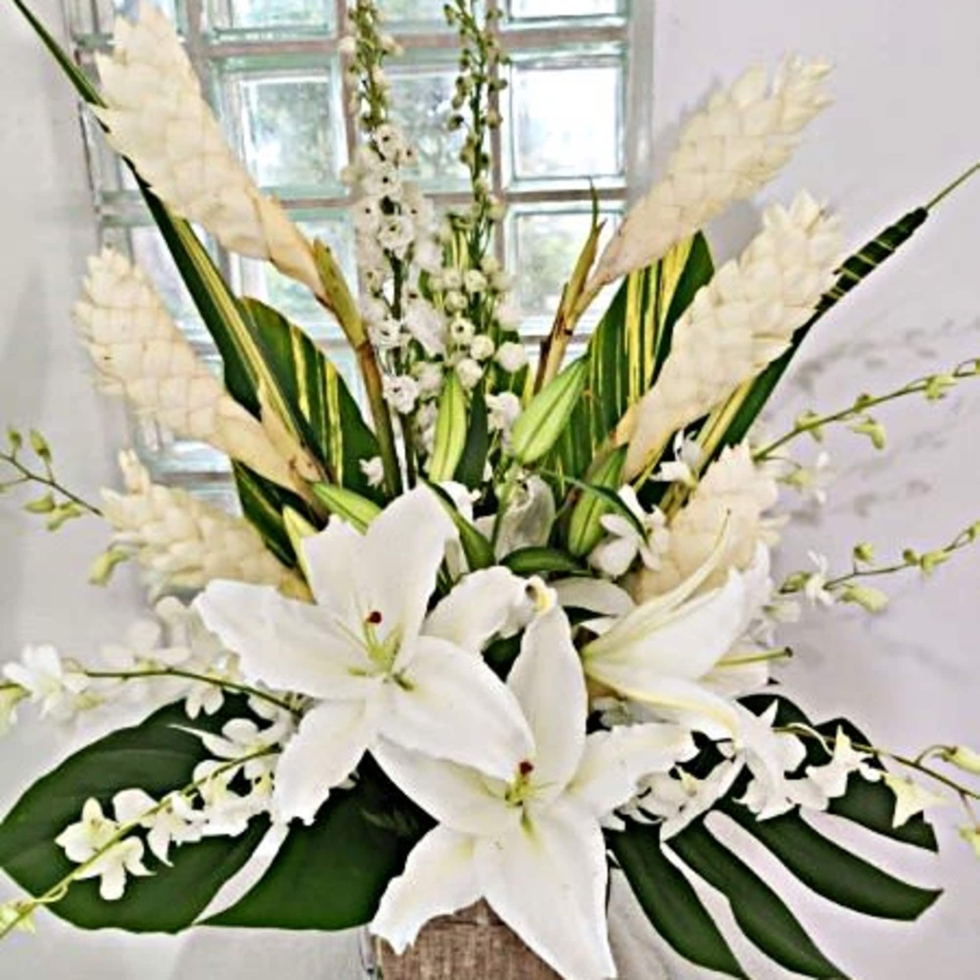 White lilies and orchids in a square glass vase with large green leaves