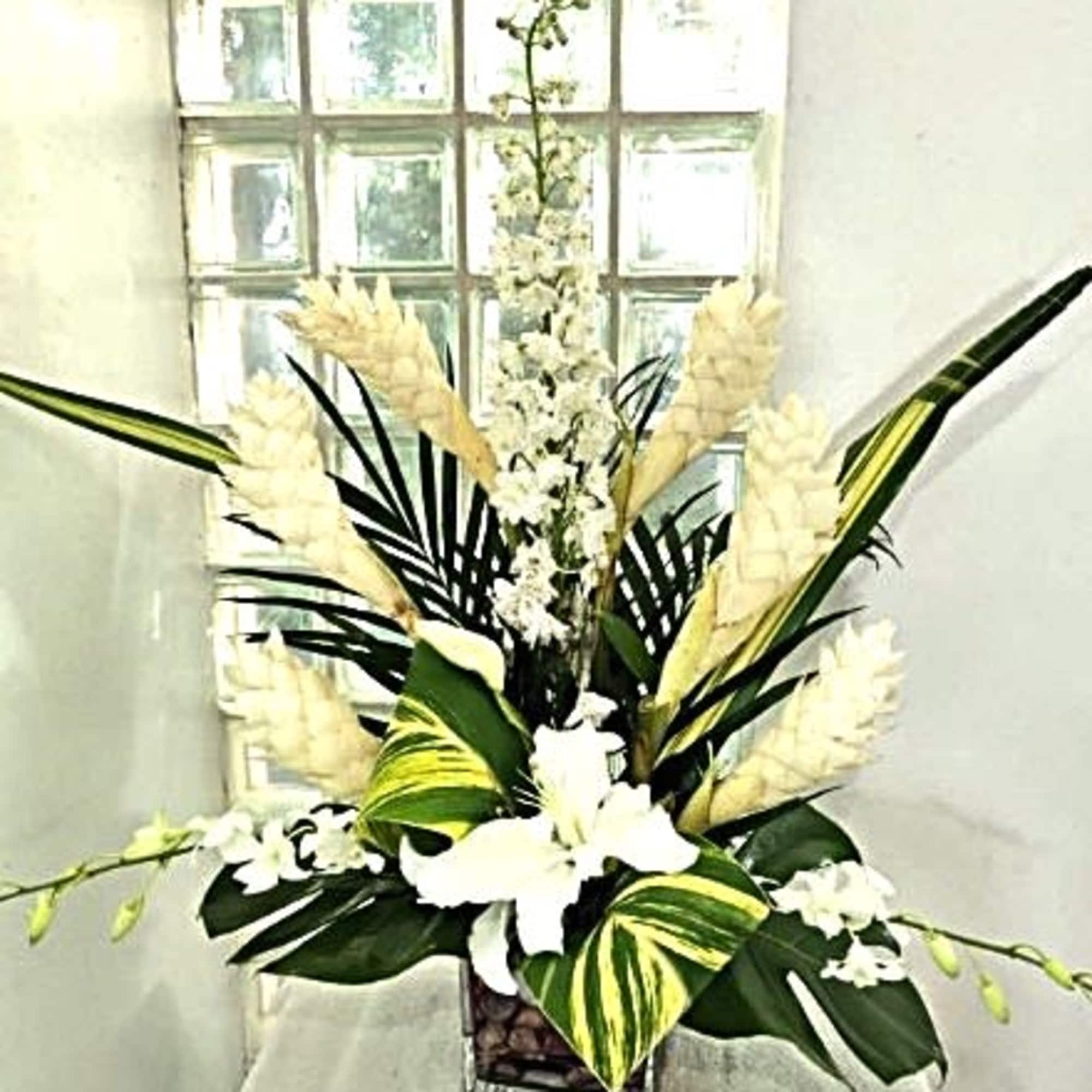 Tall white floral arrangement with tropical leaves in a square vase