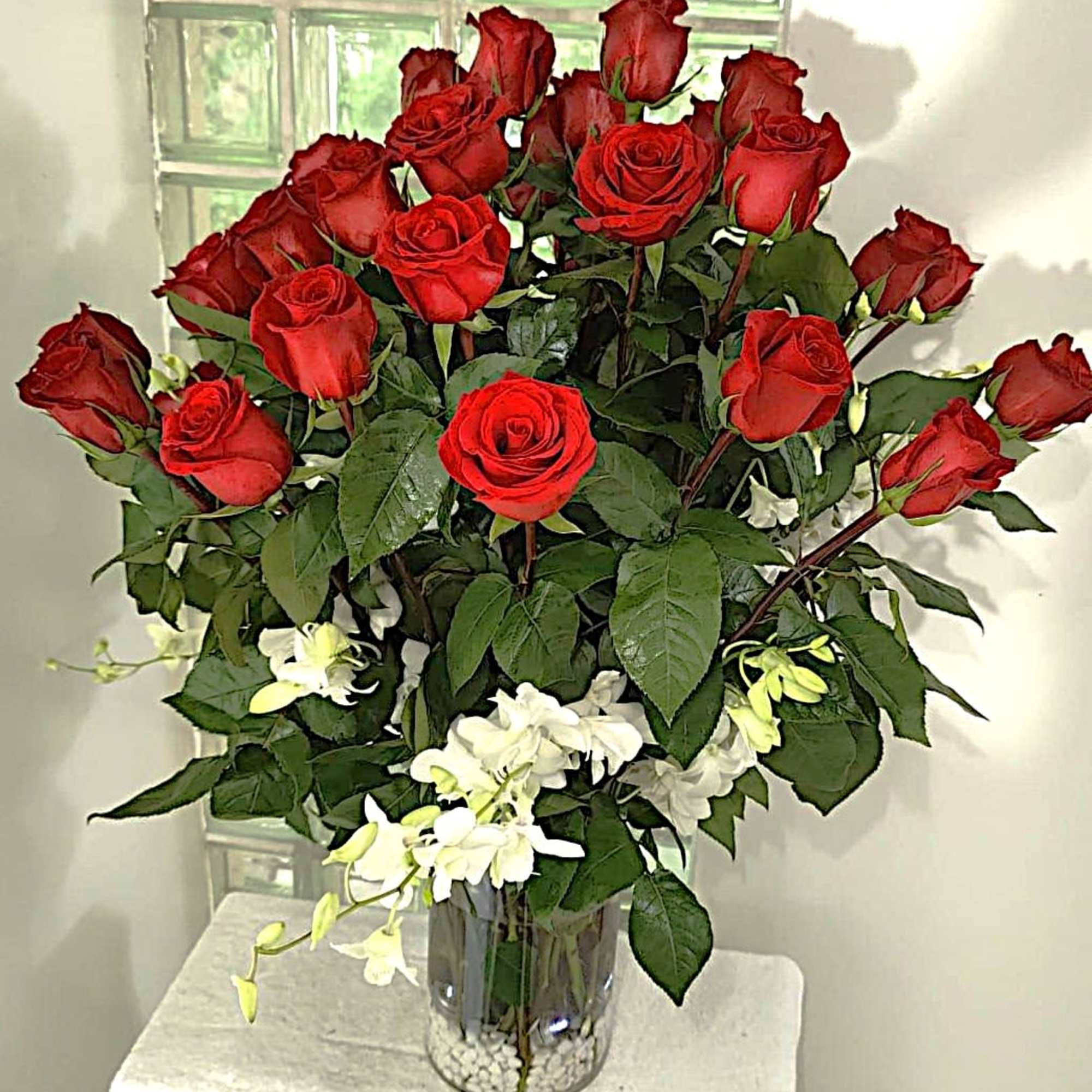 Red roses arranged in a clear glass vase with white flowers