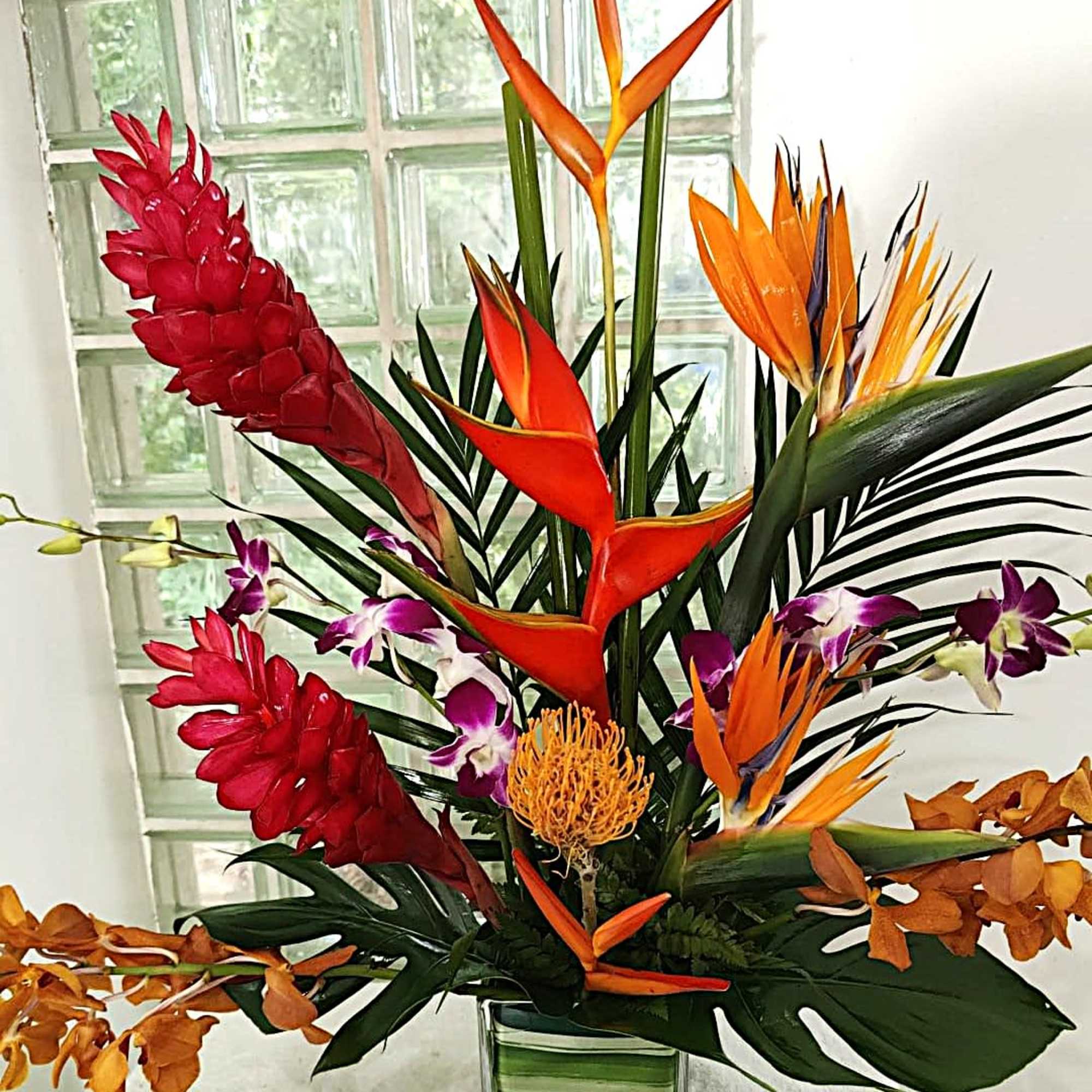 Tropical flower arrangement with orange bird-of-paradise and red ginger in a glass vase