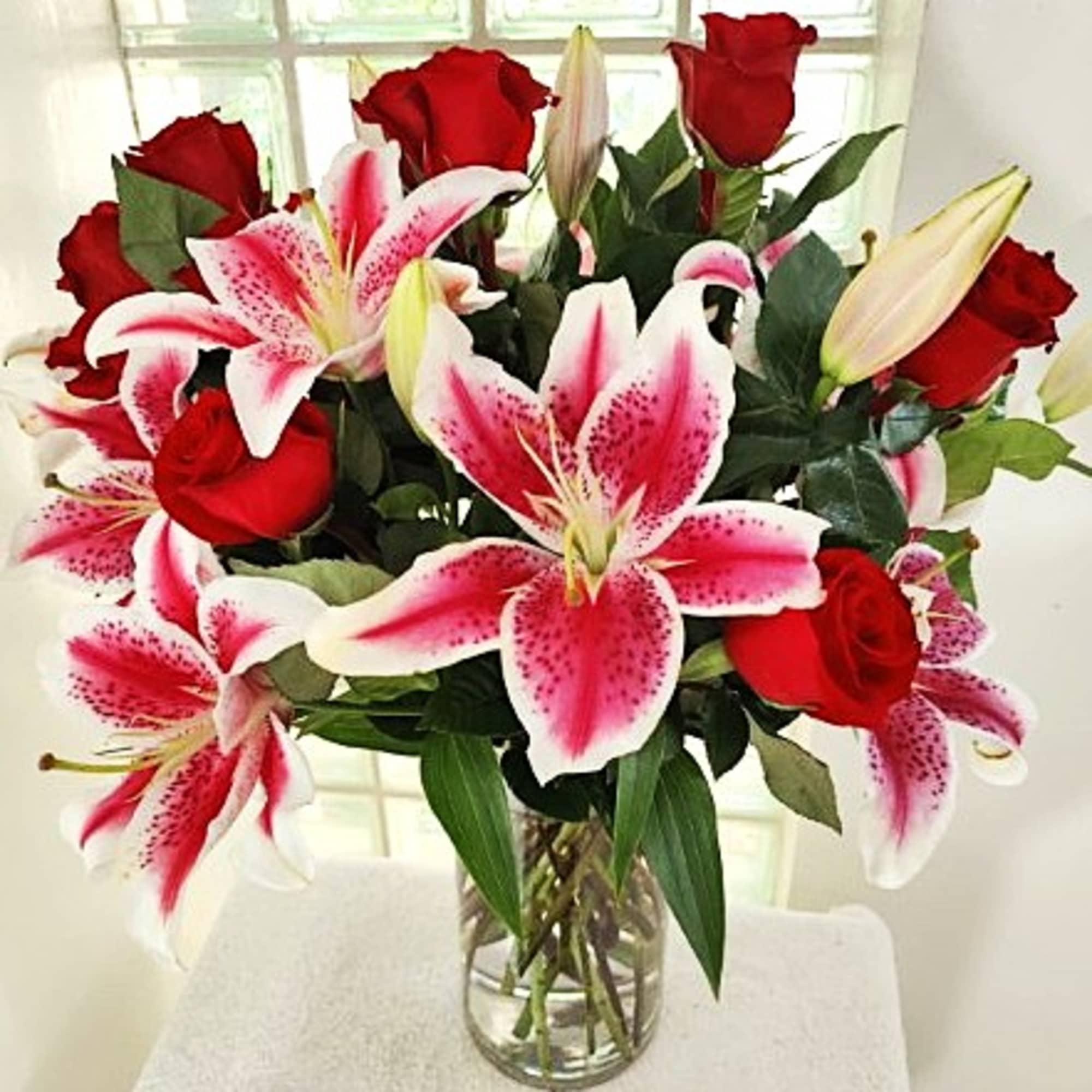 Bouquet of red roses and pink stargazer lilies in a clear glass vase