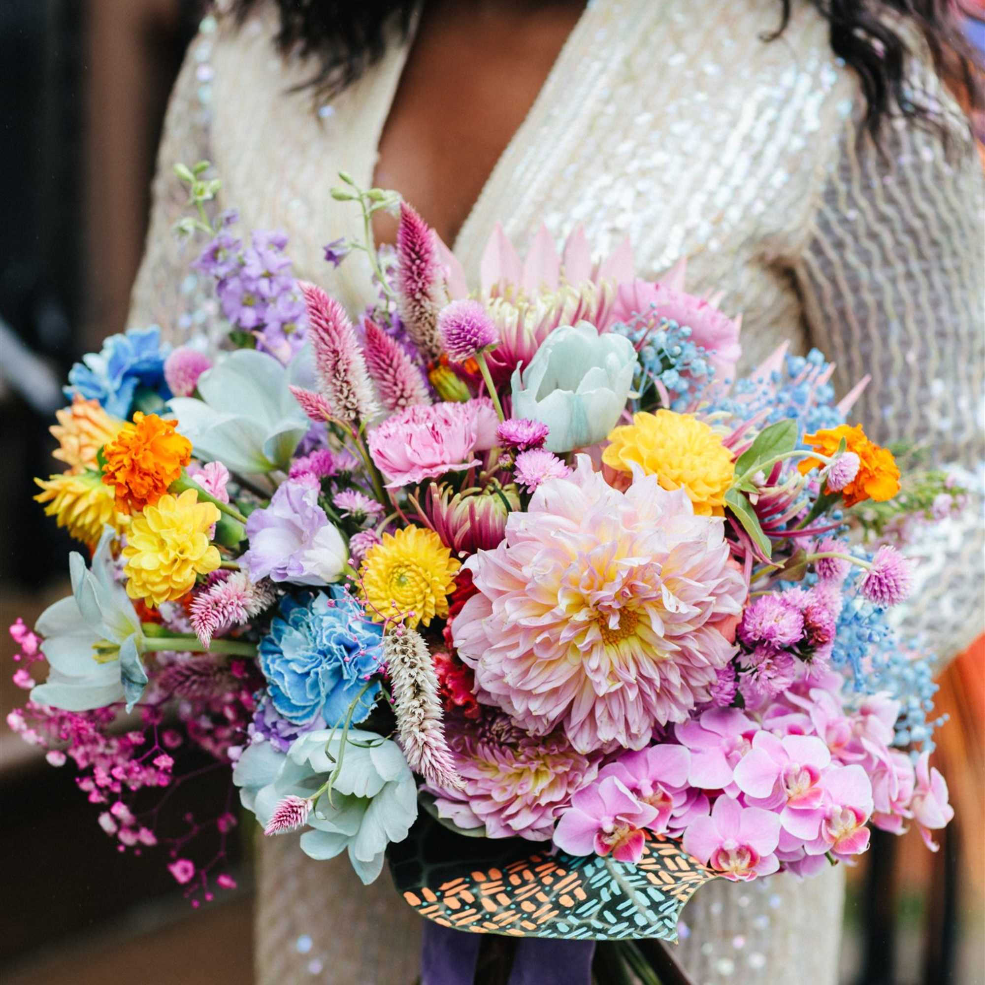 Woman holding a colorful bouquet with orchids, dahlias, and other mixed flowers