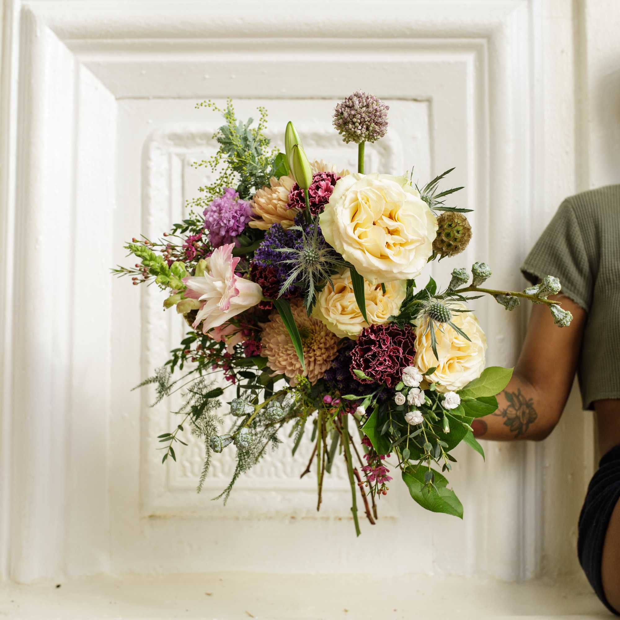 Handheld bouquet of cream, pink, and purple flowers
