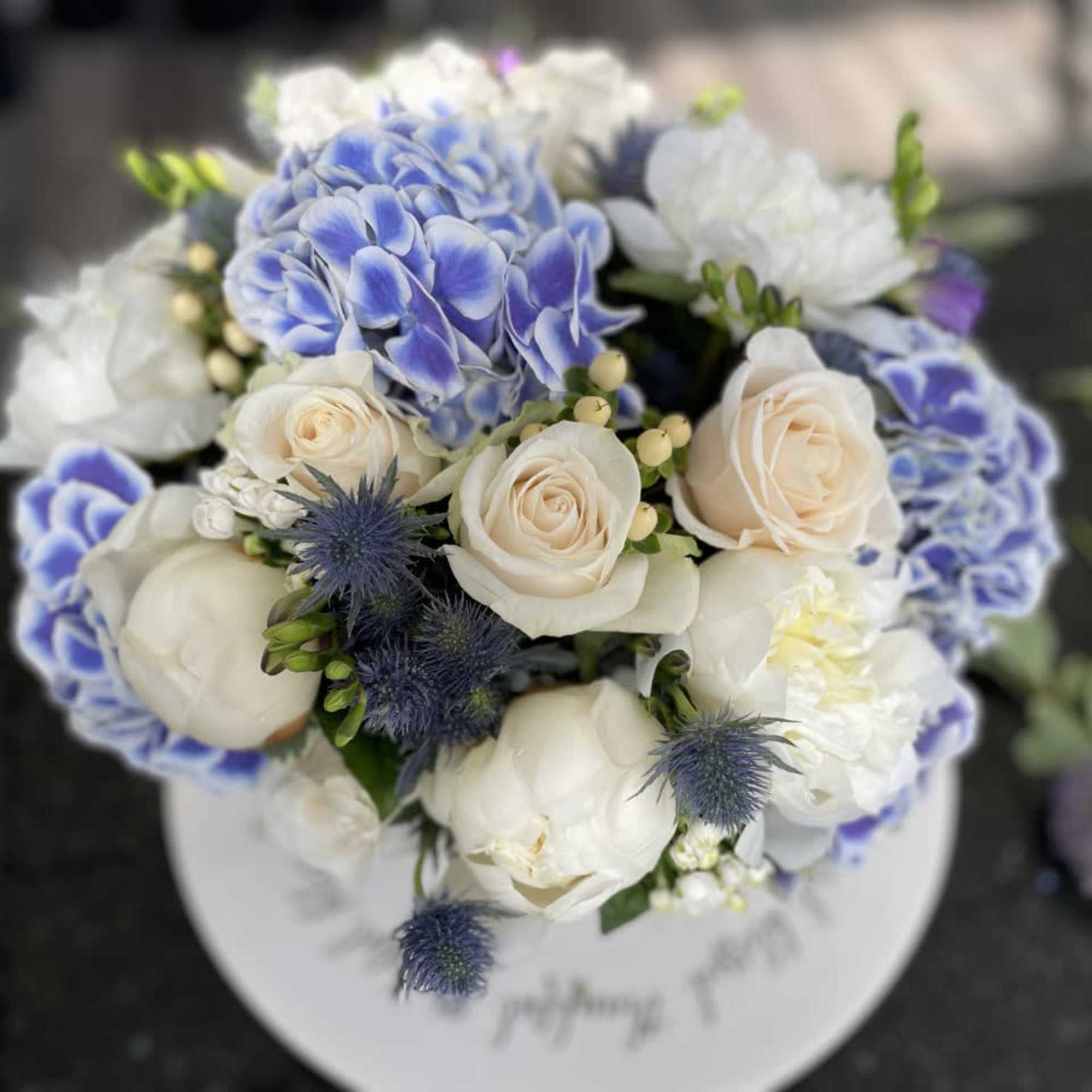 Round bouquet of white and blue flowers in a white box