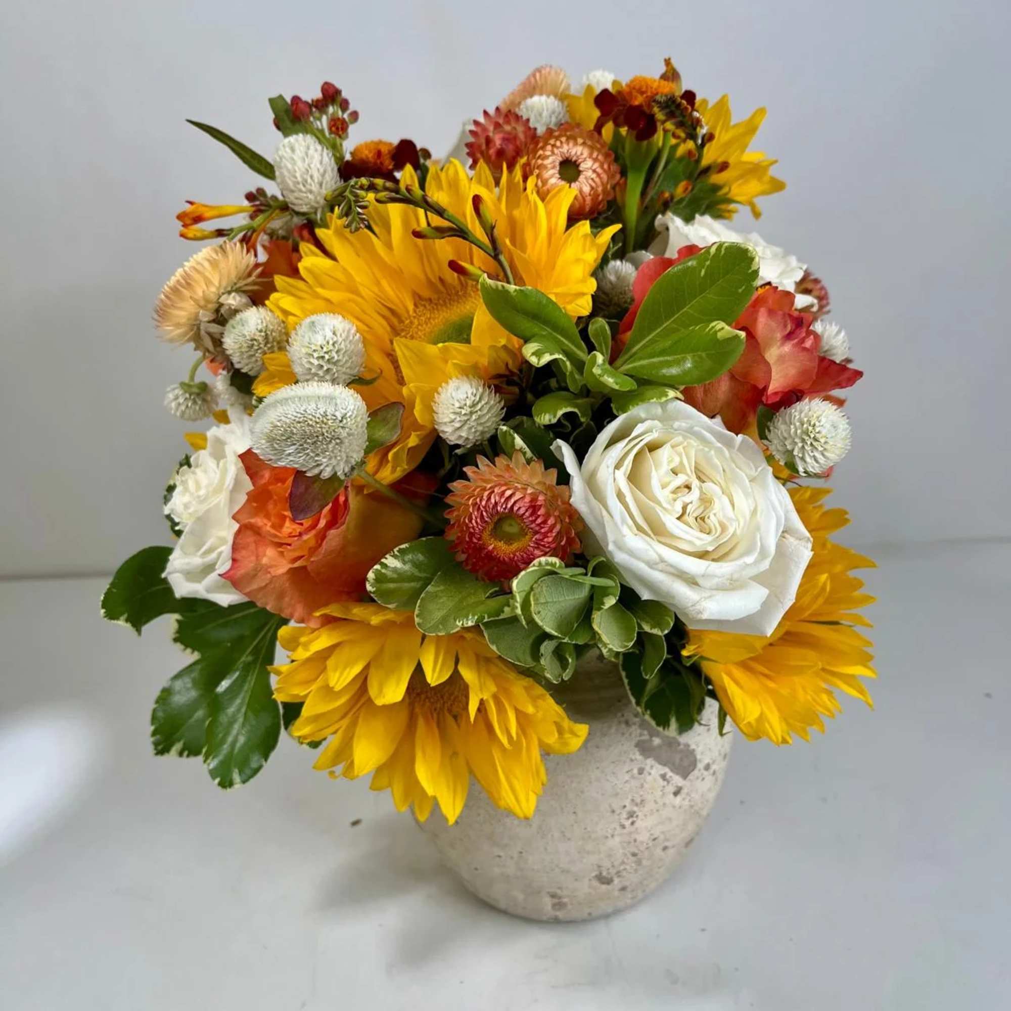 Mixed bouquet of yellow sunflowers, white roses, and orange blooms in a stone vase