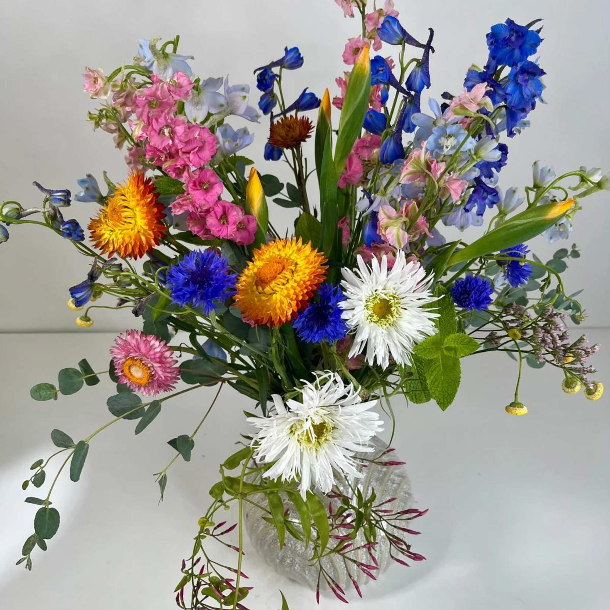 Colorful mixed bouquet with blue, pink, white, and yellow flowers in a clear vase