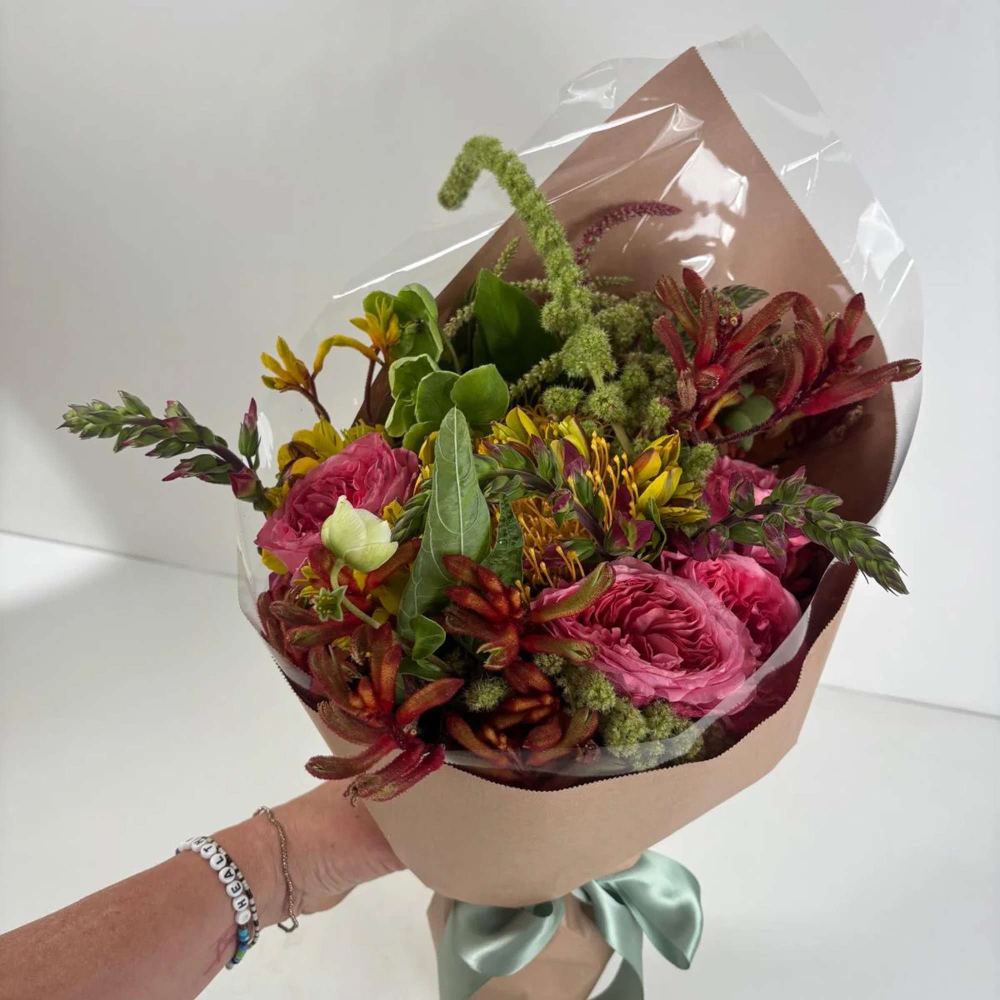 Handheld bouquet of pink roses and mixed blooms wrapped in brown paper and clear plastic