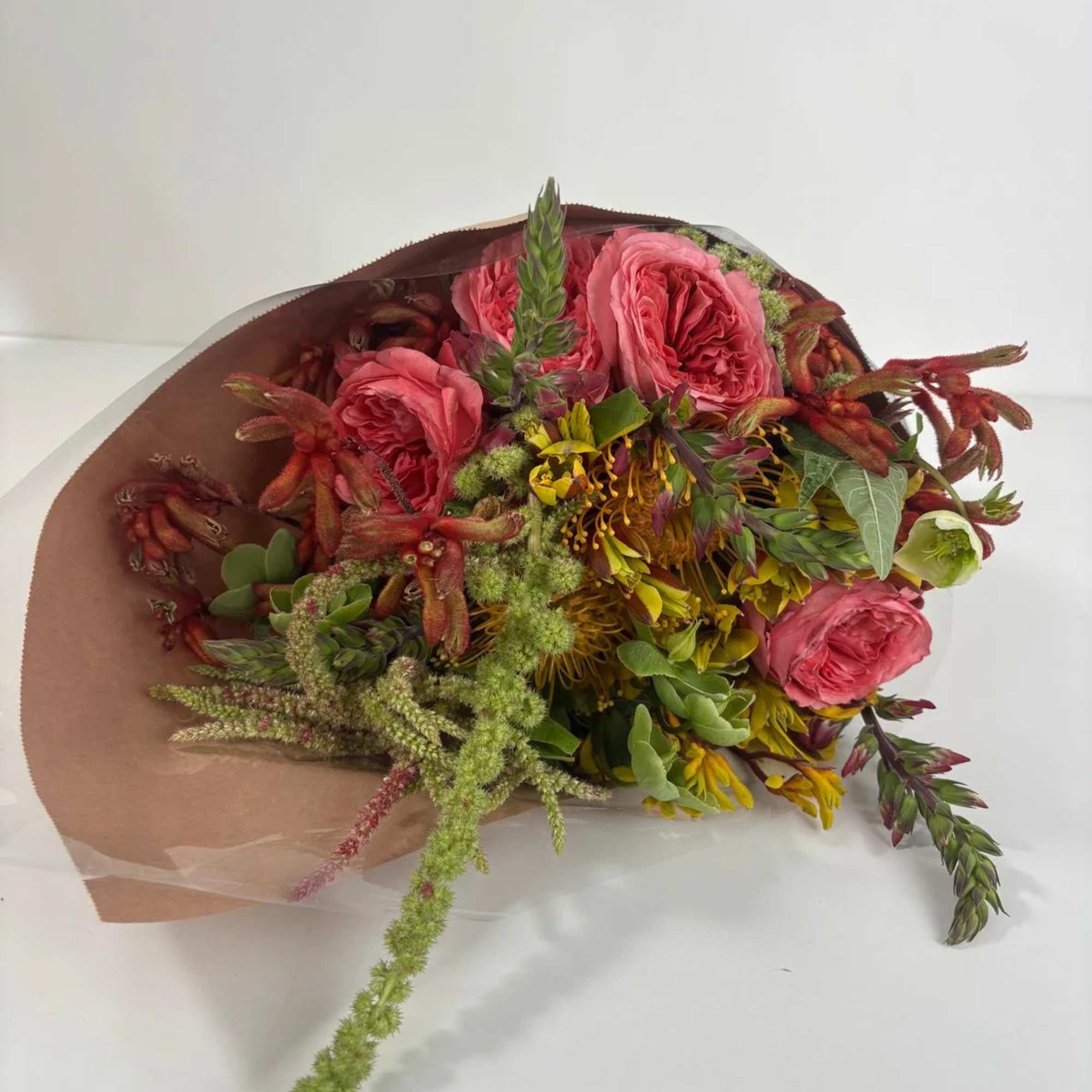 Bouquet of pink roses with mixed yellow and green flowers wrapped in brown paper