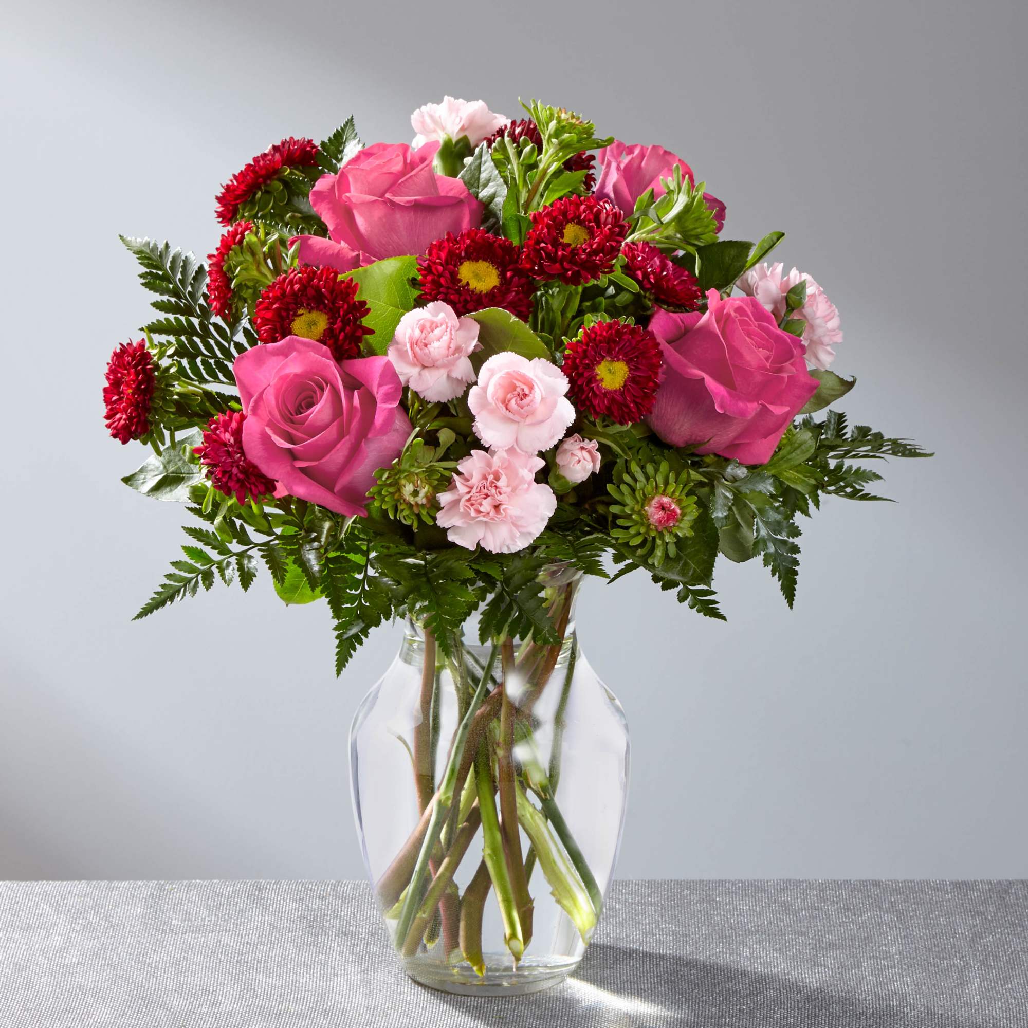 Pink roses and red daisy flowers arranged in a clear glass vase.