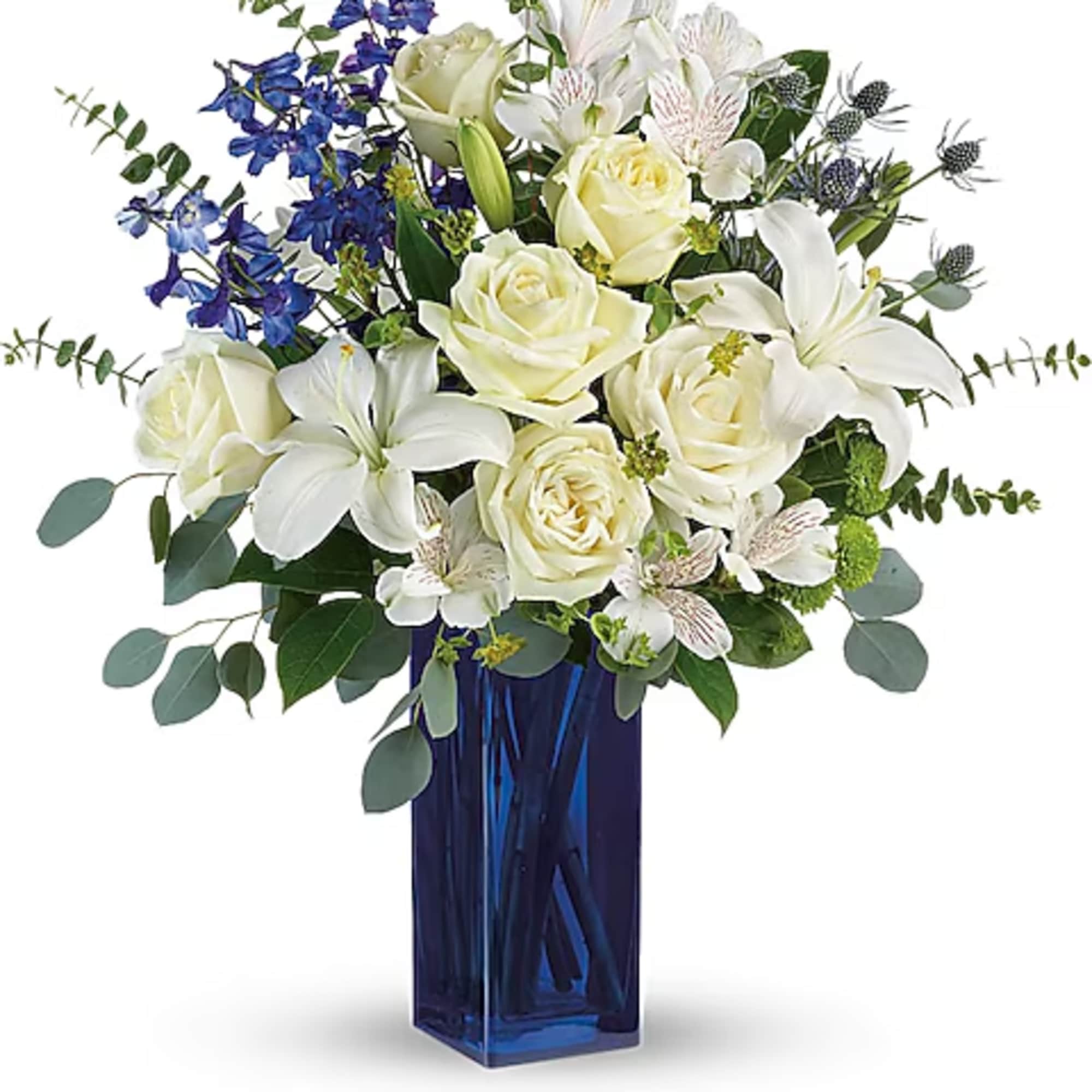 White roses and lilies arranged in a blue glass vase with blue flowers