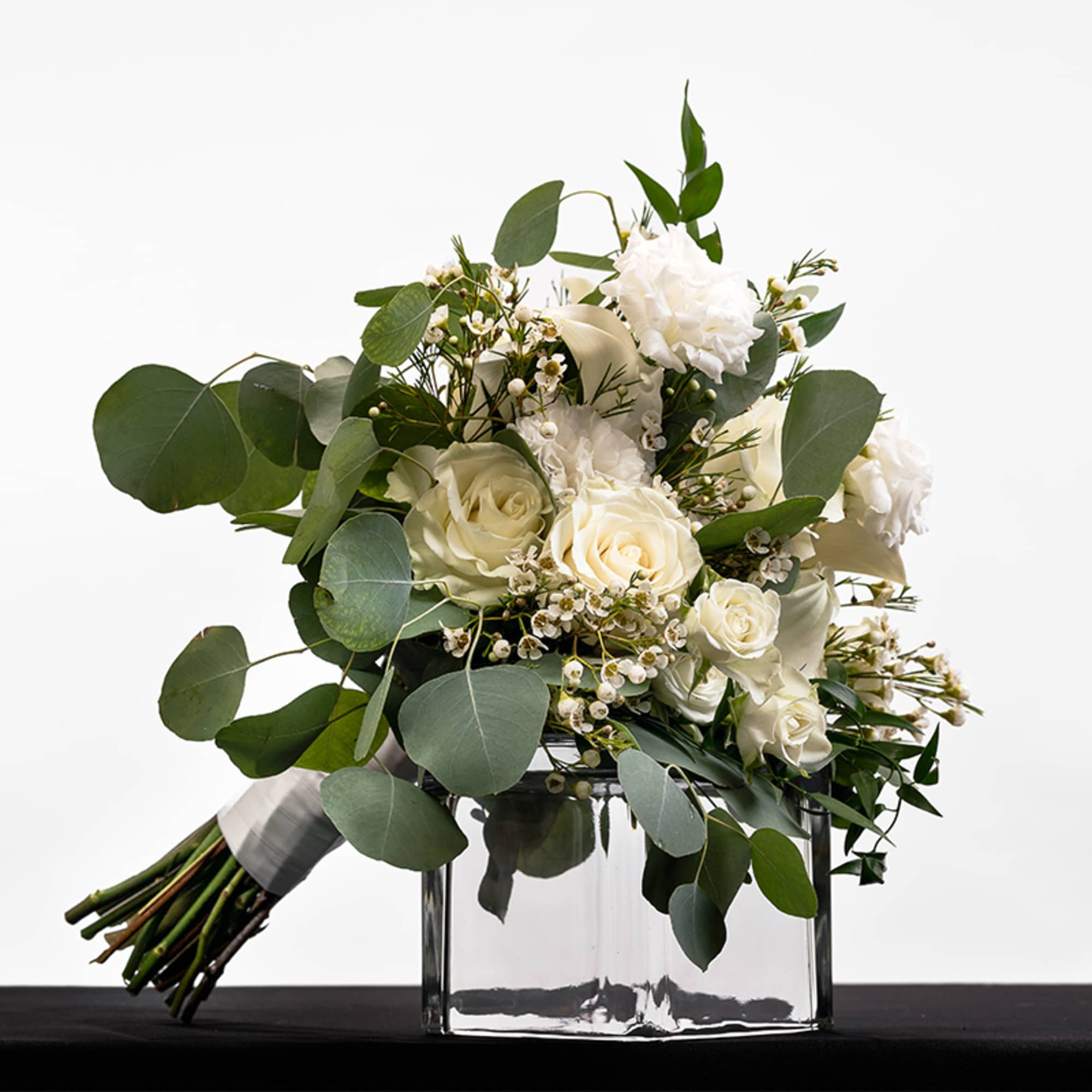 Hand-tied bouquet of white roses and blooms with eucalyptus resting on a glass cube vase