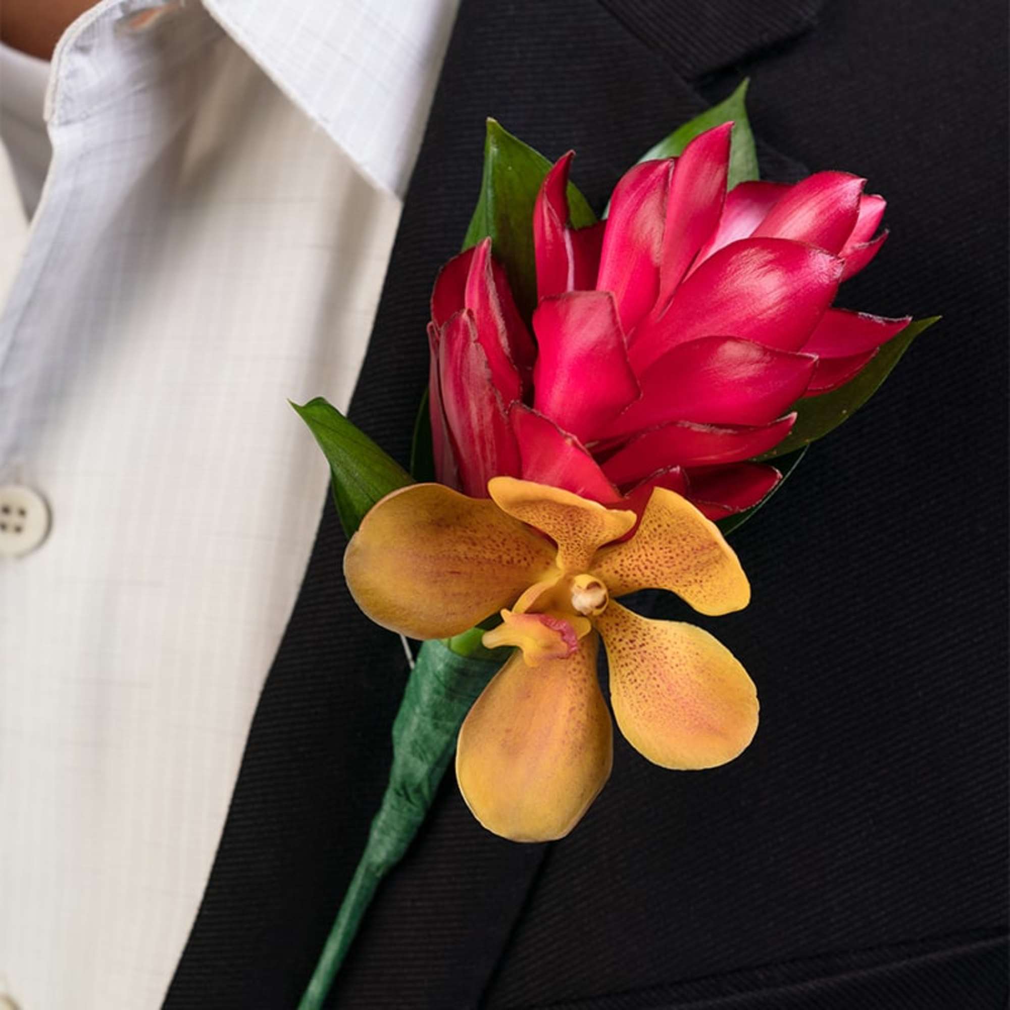 Tropical red and yellow orchid boutonniere pinned to a black suit jacket with white dress shirt.