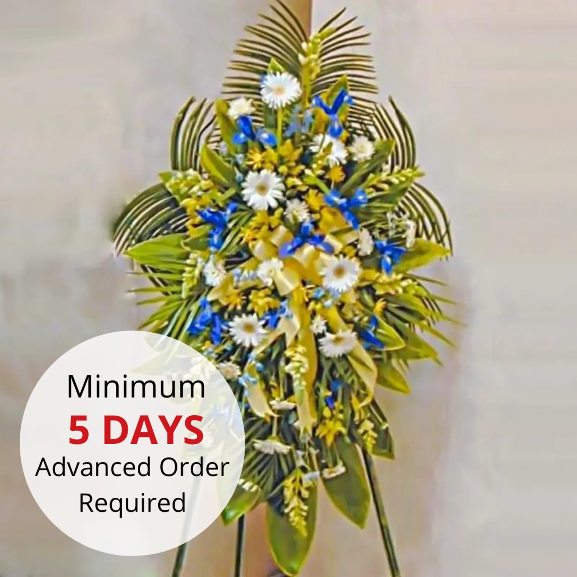 Tall standing spray with white daisies, blue flowers, and yellow ribbon on a metal easel.