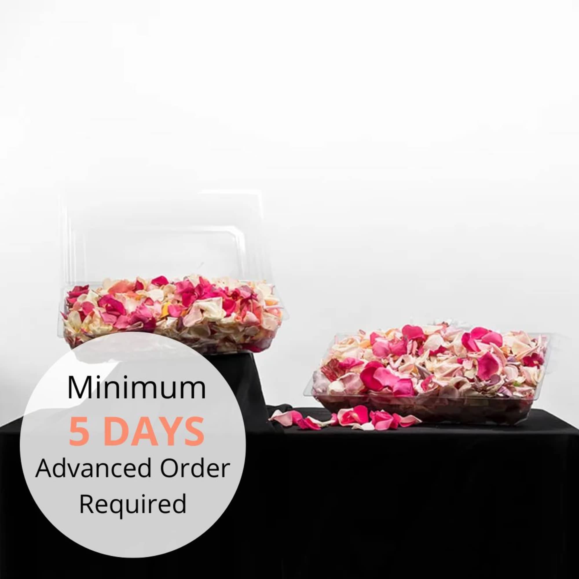 Two plastic containers filled with mixed pink and ivory rose petals on a black covered table