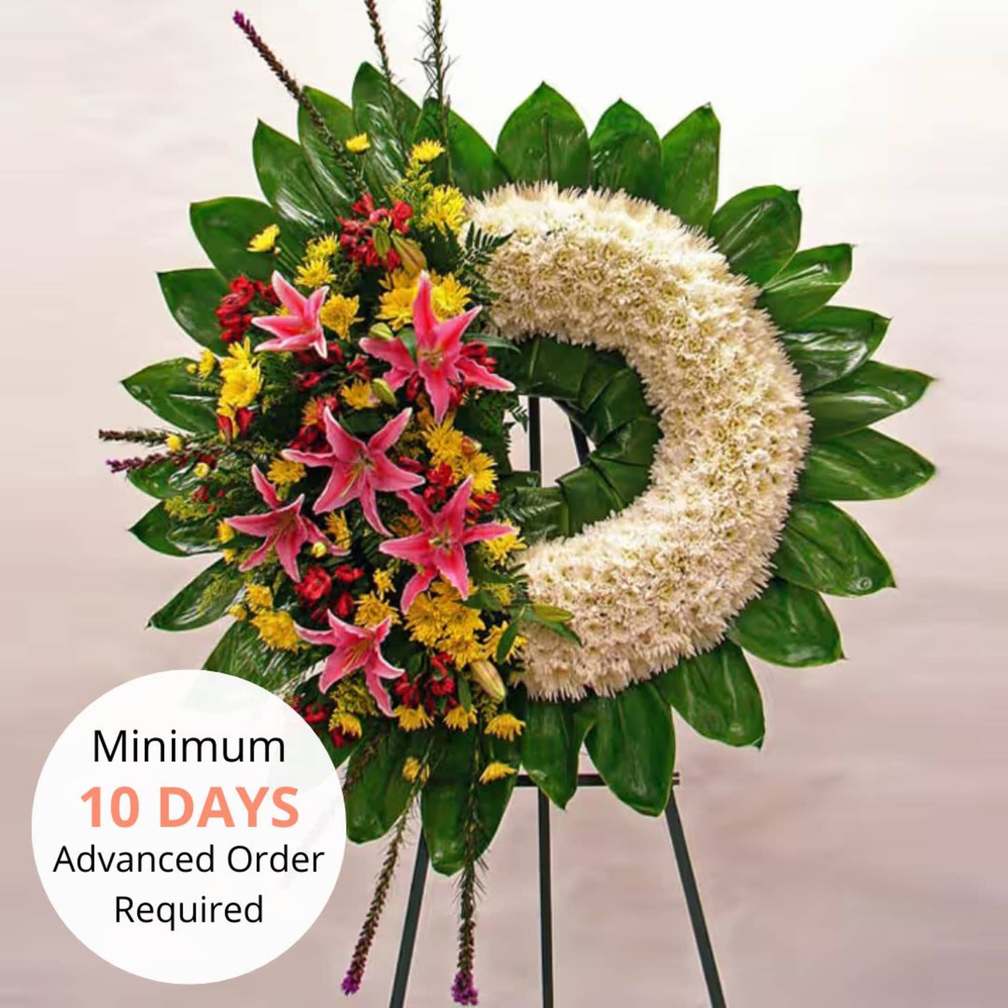 Standing wreath of white flowers with pink lilies and yellow accents on a metal easel.