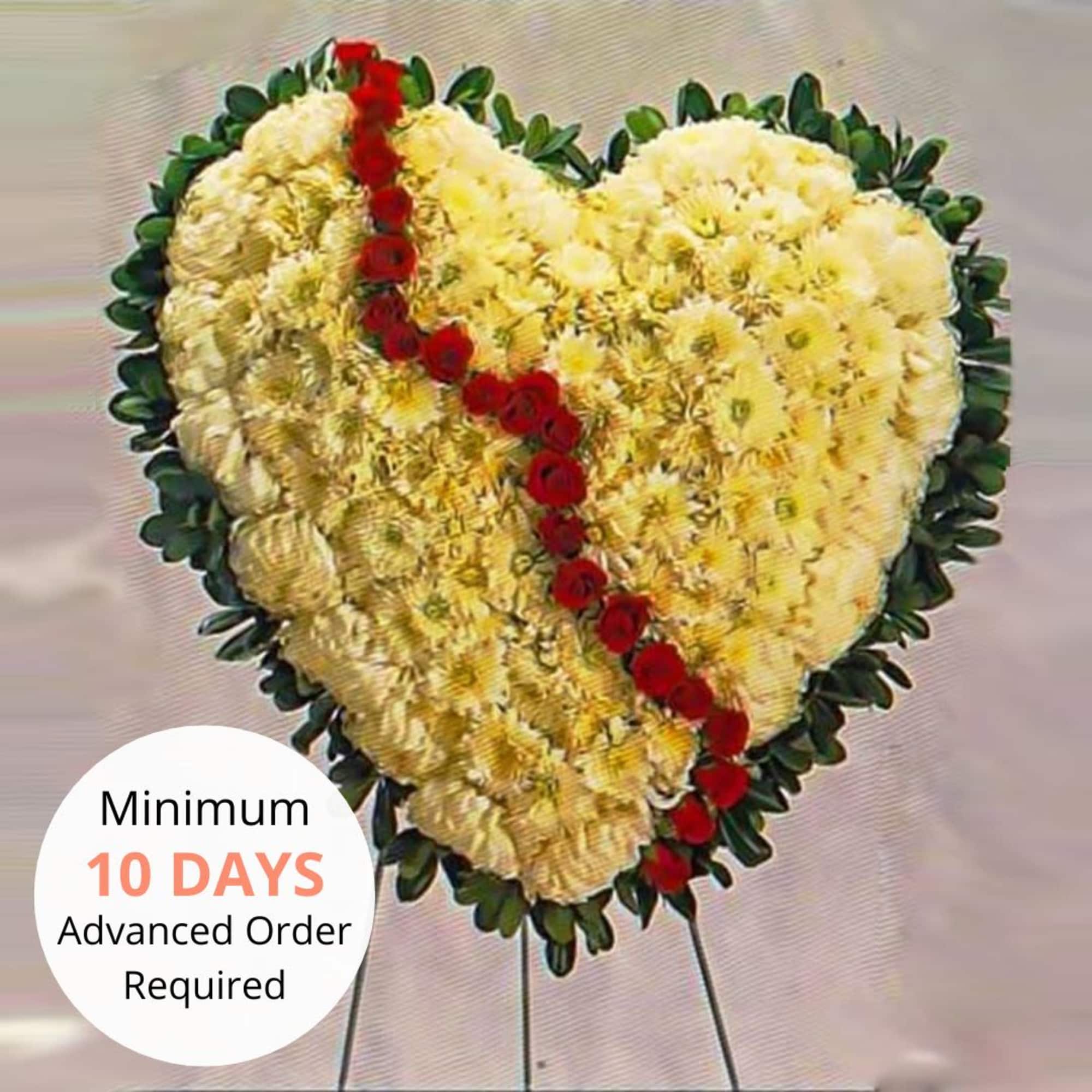 Heart-shaped standing floral tribute of cream flowers with a diagonal line of red roses.