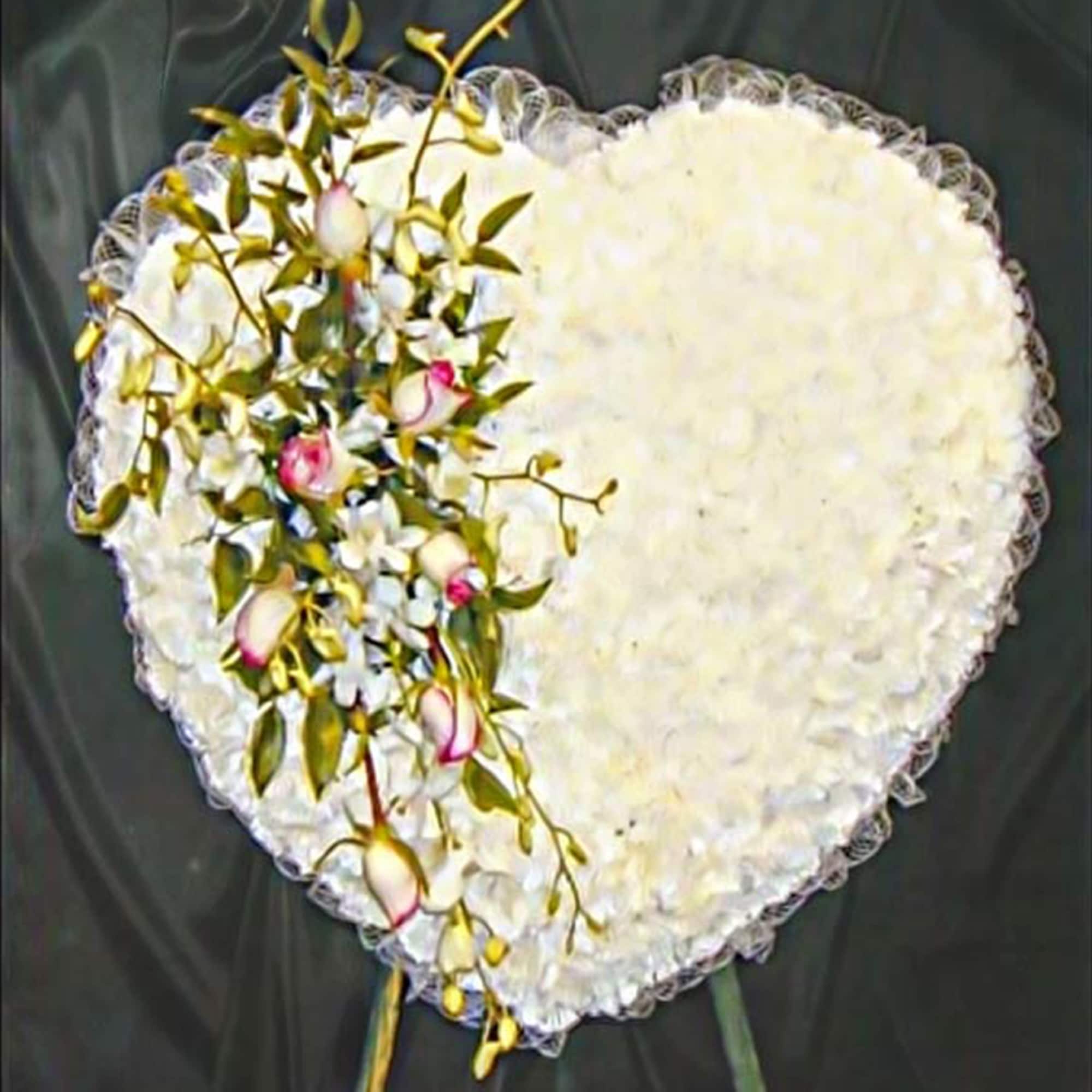 Heart-shaped white floral tribute with pink rosebuds and white accent flowers on one side