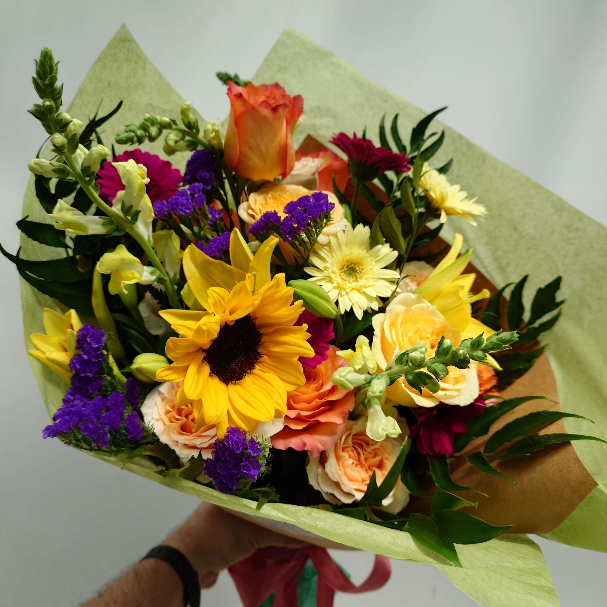 Mixed bouquet with sunflowers, roses, and purple filler flowers wrapped in paper