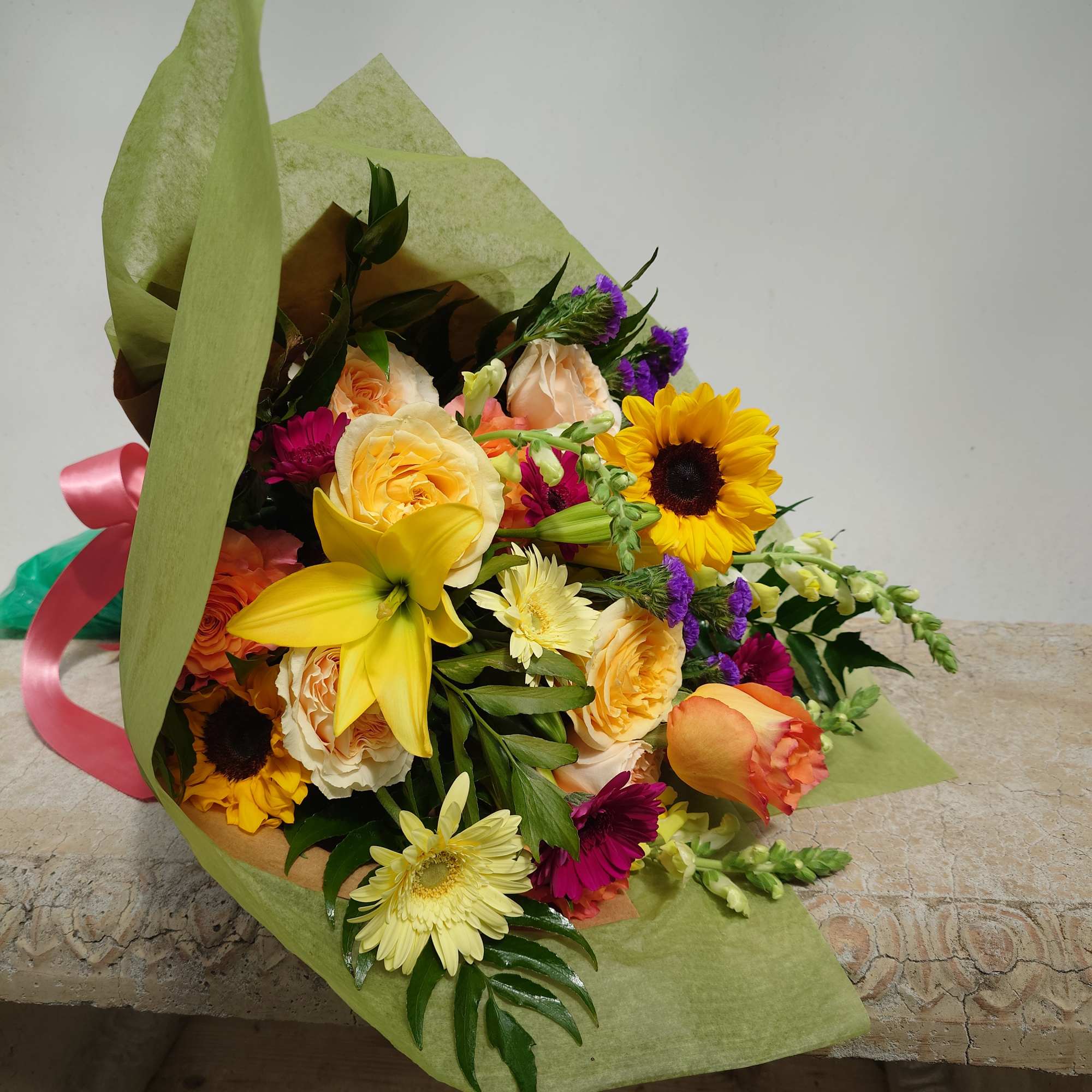 Mixed bouquet with yellow lilies, roses, sunflowers, and daisies wrapped in green paper