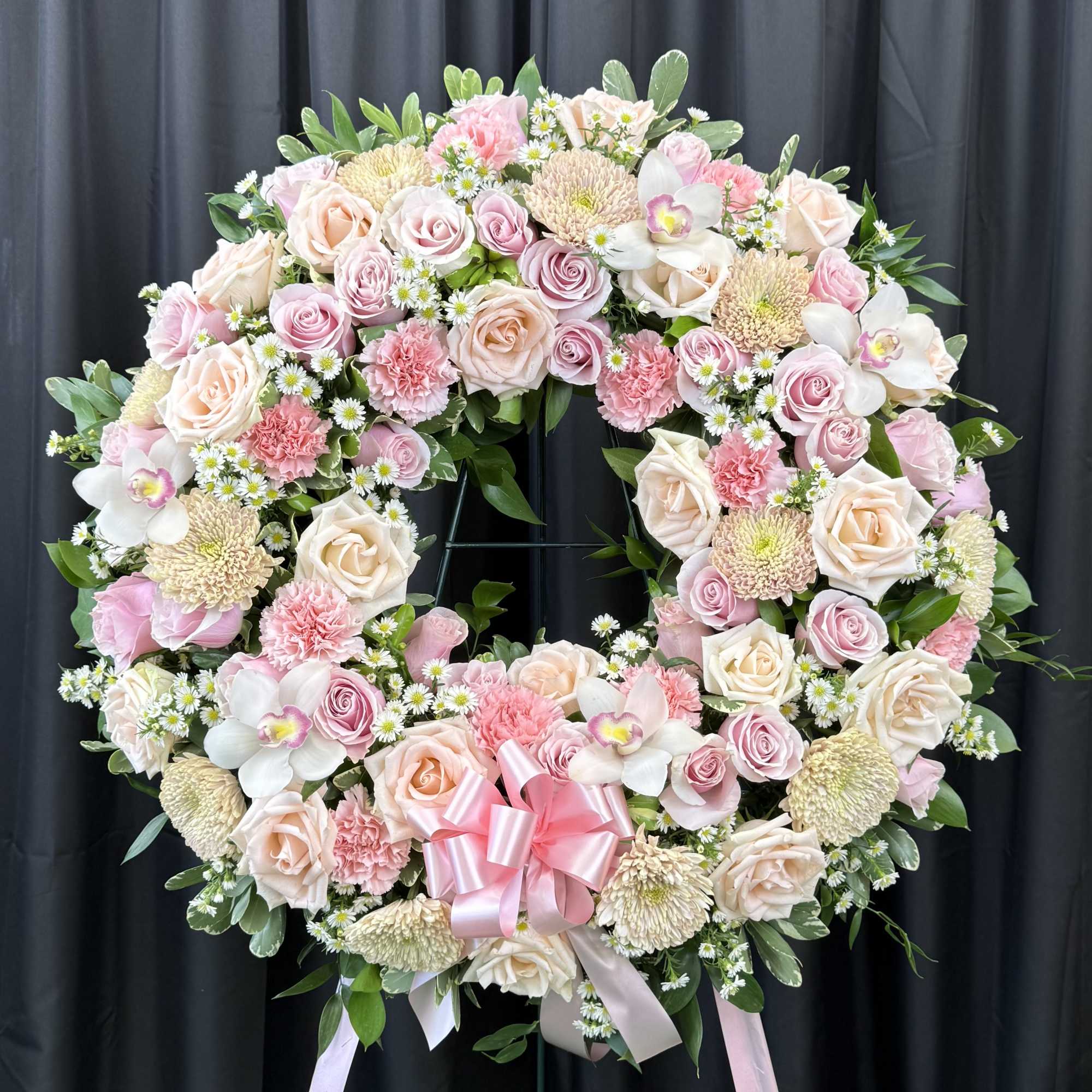 Large pink and cream floral wreath on a stand with a pink ribbon bow
