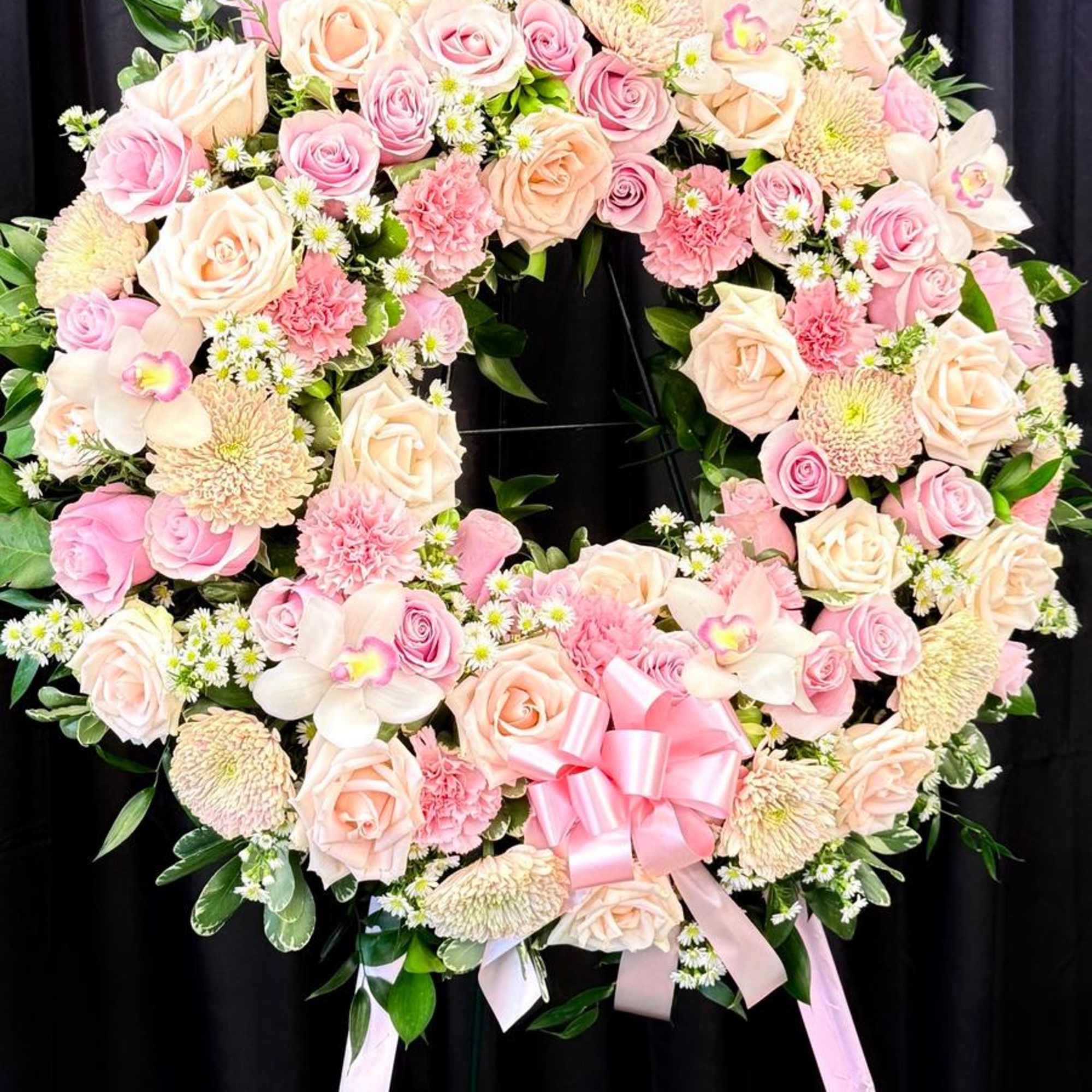Heart-shaped floral wreath with pink and cream roses and a pink ribbon bow
