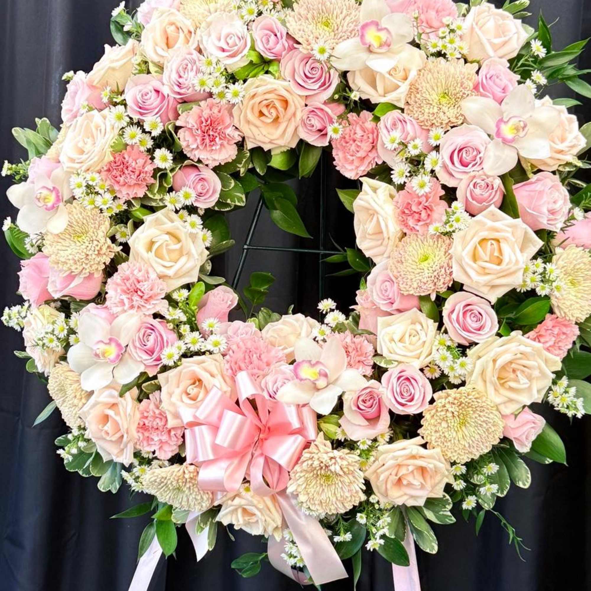 Heart-shaped floral wreath with pink and cream roses and a pink ribbon bow