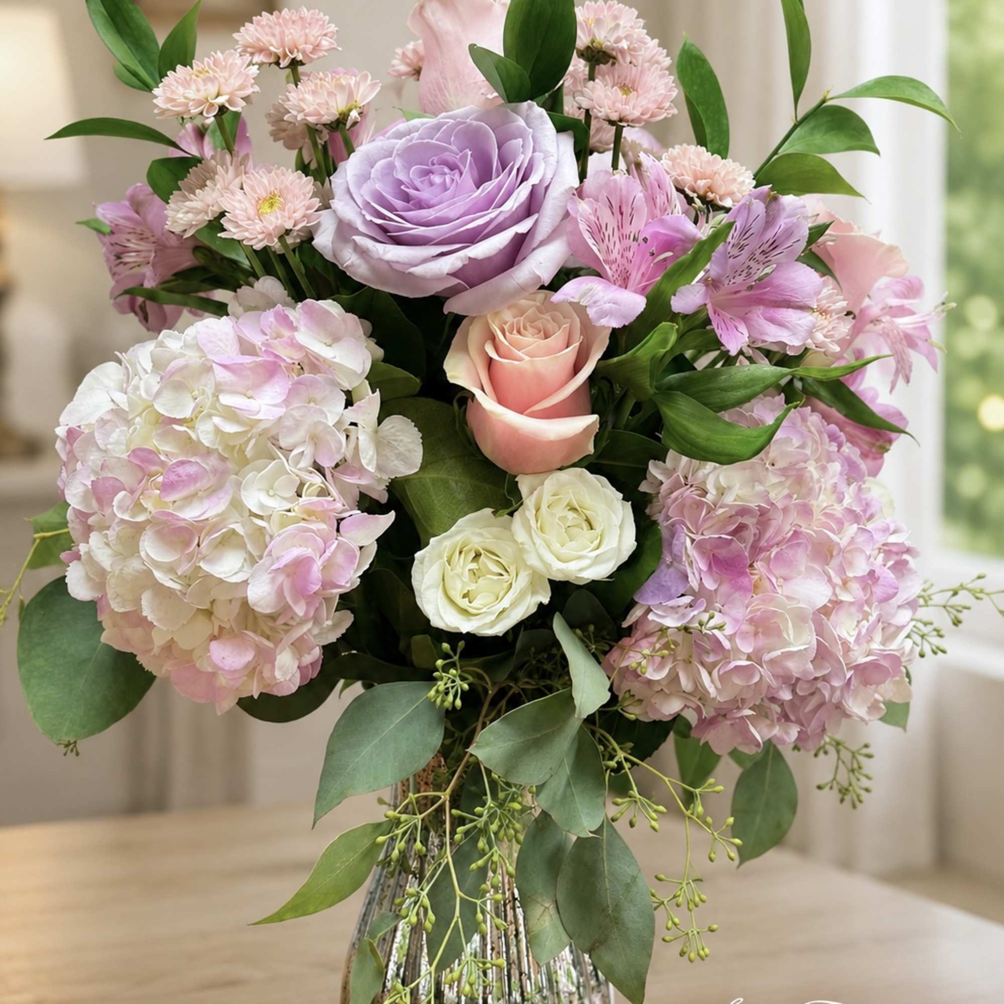 Pink and lavender floral arrangement in a glass vase with roses and hydrangeas