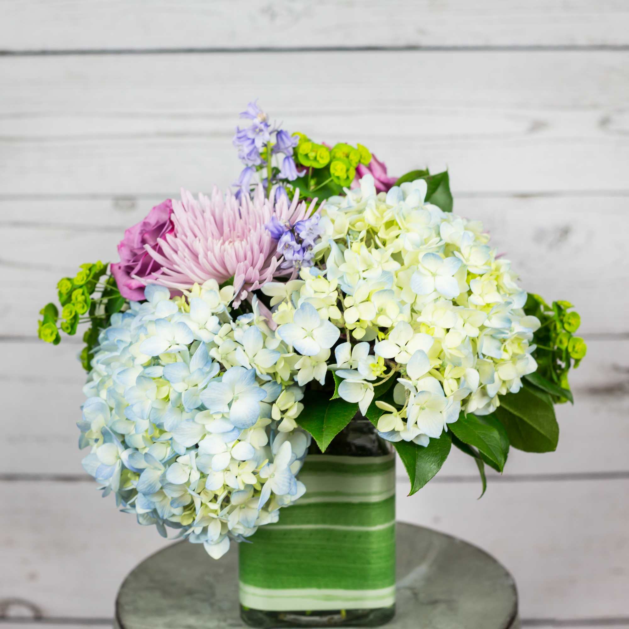 Bouquet of pastel hydrangeas and pink flowers in a green glass vase