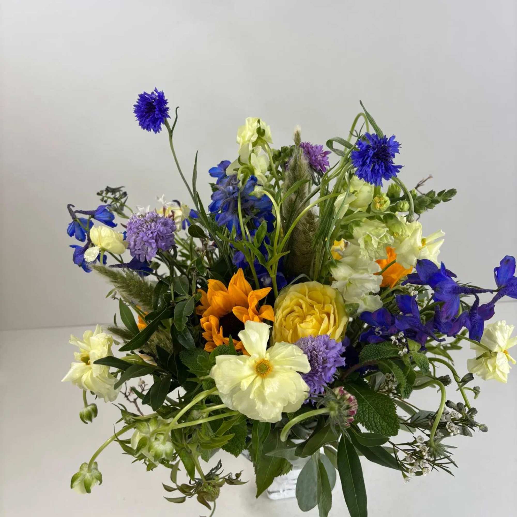 Mixed bouquet with blue, yellow, and purple flowers in a clear vase