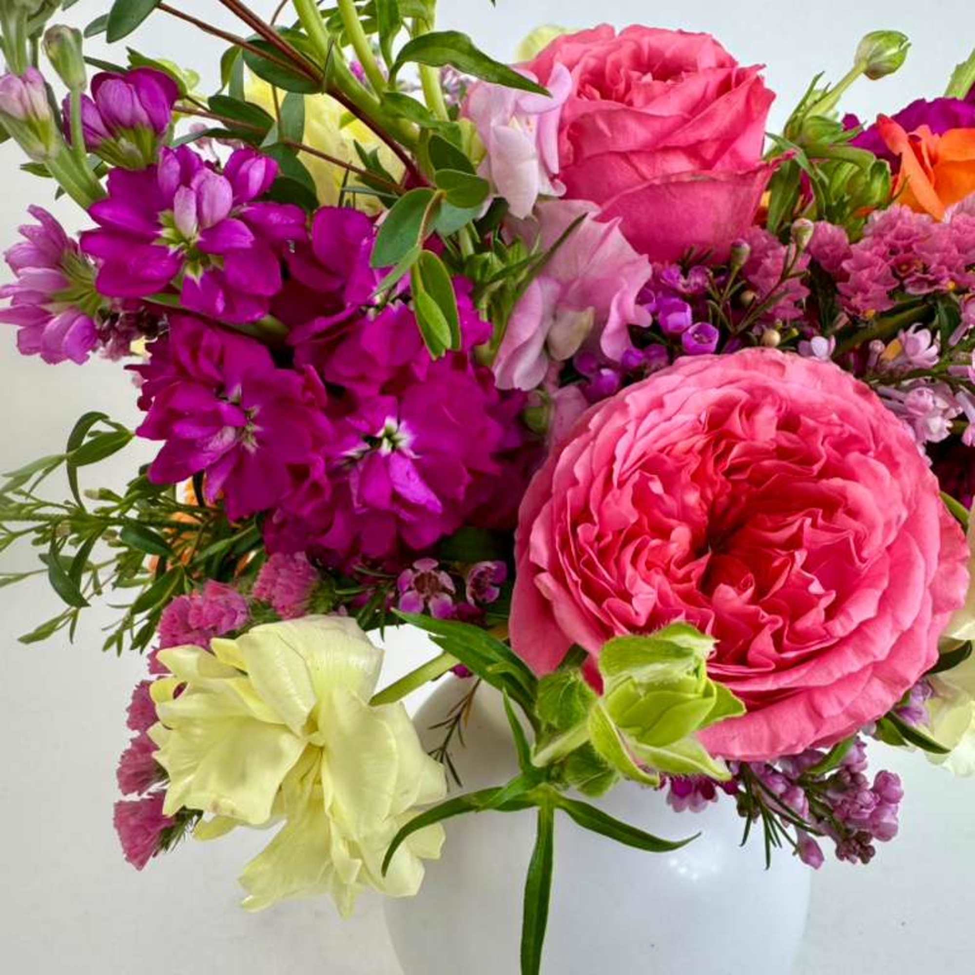 Bright mixed bouquet of pink, purple, and pale yellow flowers in a white vase