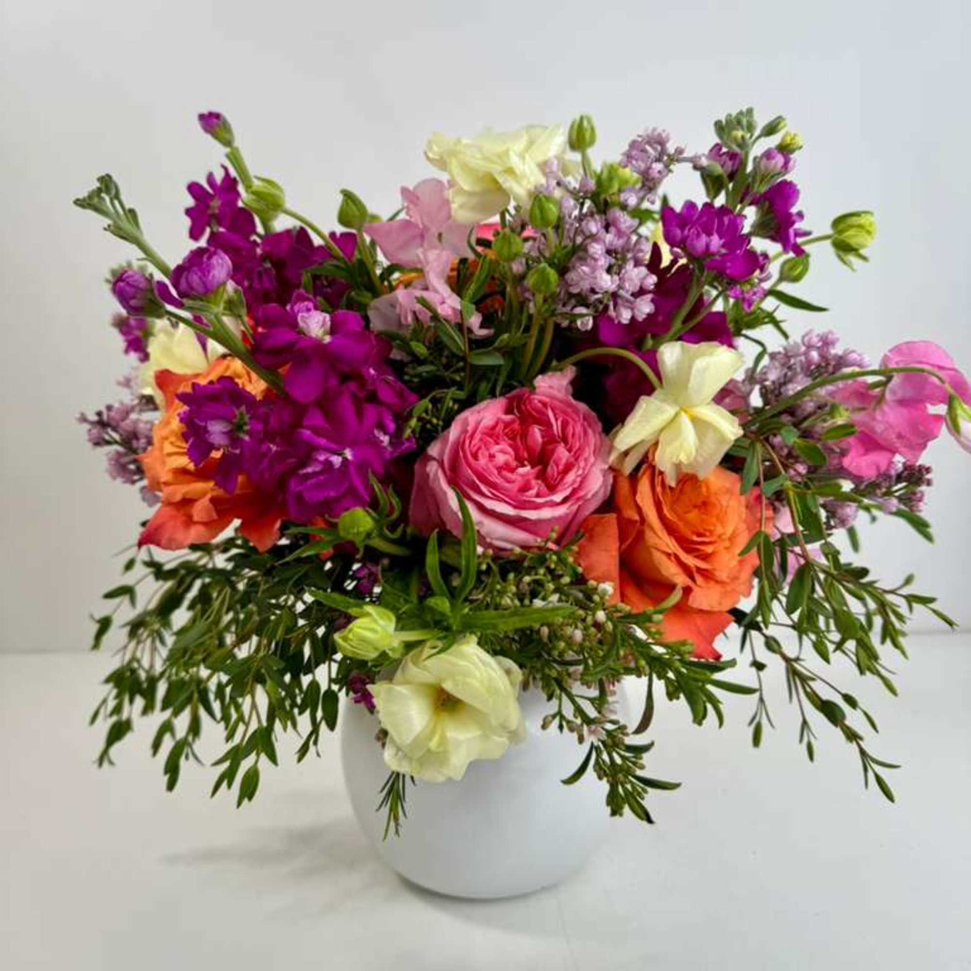 Mixed bouquet of pink, purple, orange, and cream flowers in a white vase