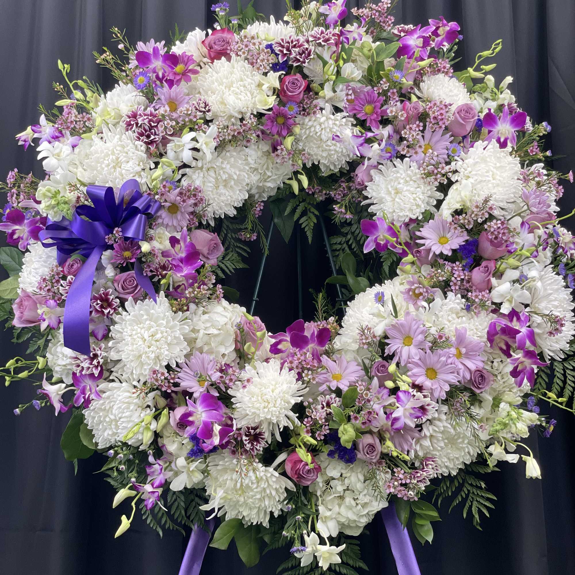 Large purple and white floral wreath with ribbon on a stand