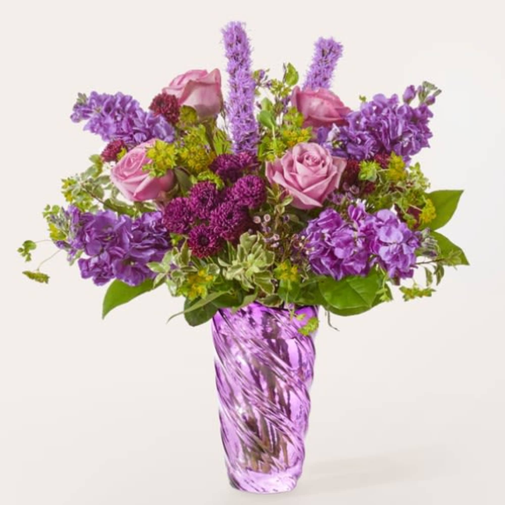 Purple and pink flower arrangement in a tall glass vase