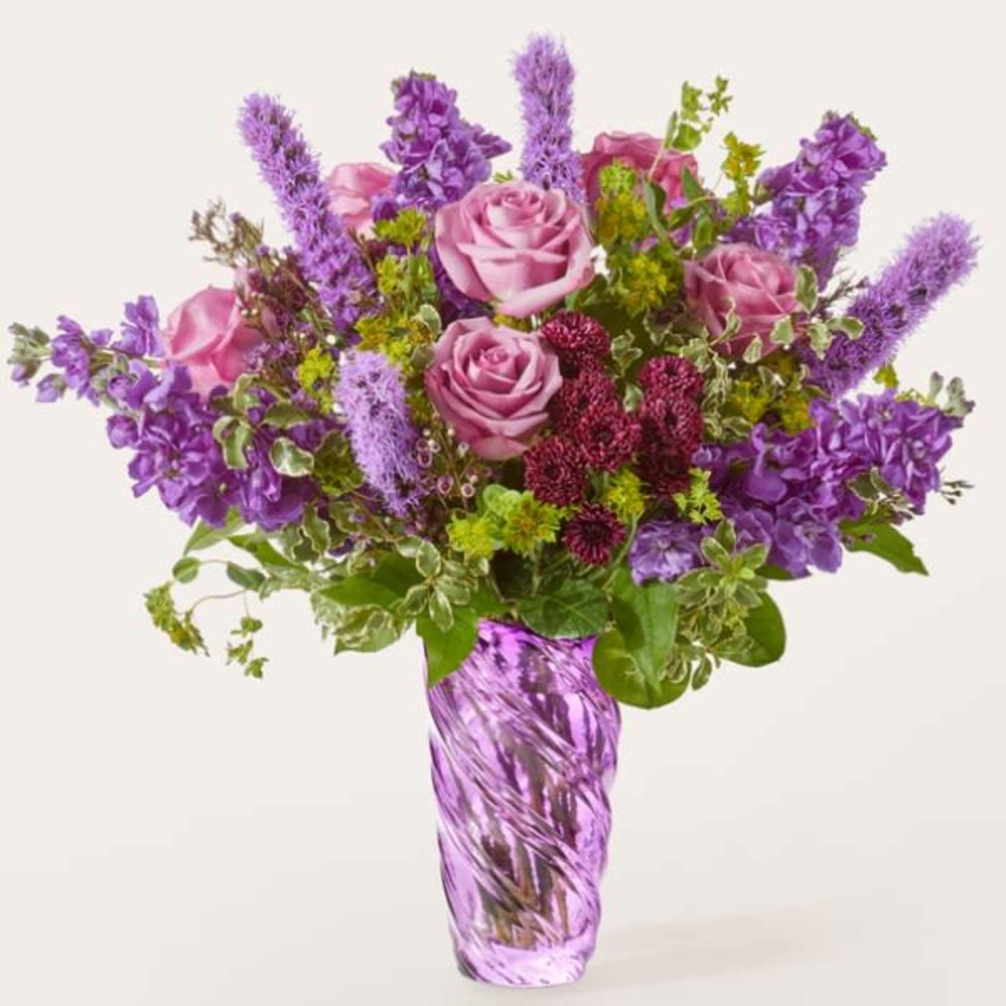 Purple and pink flower arrangement in a tall glass vase