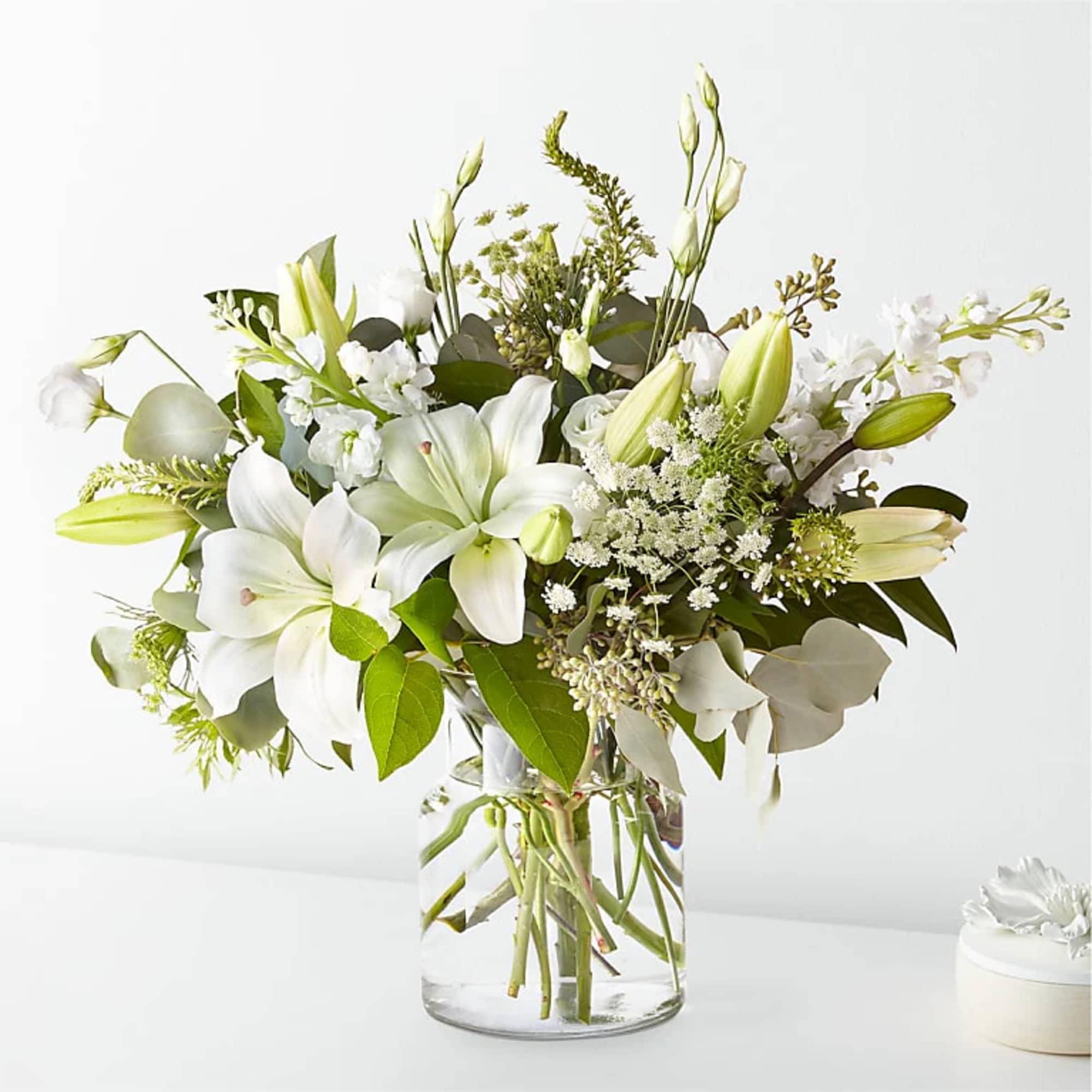 White lilies and small white flowers in a clear glass vase
