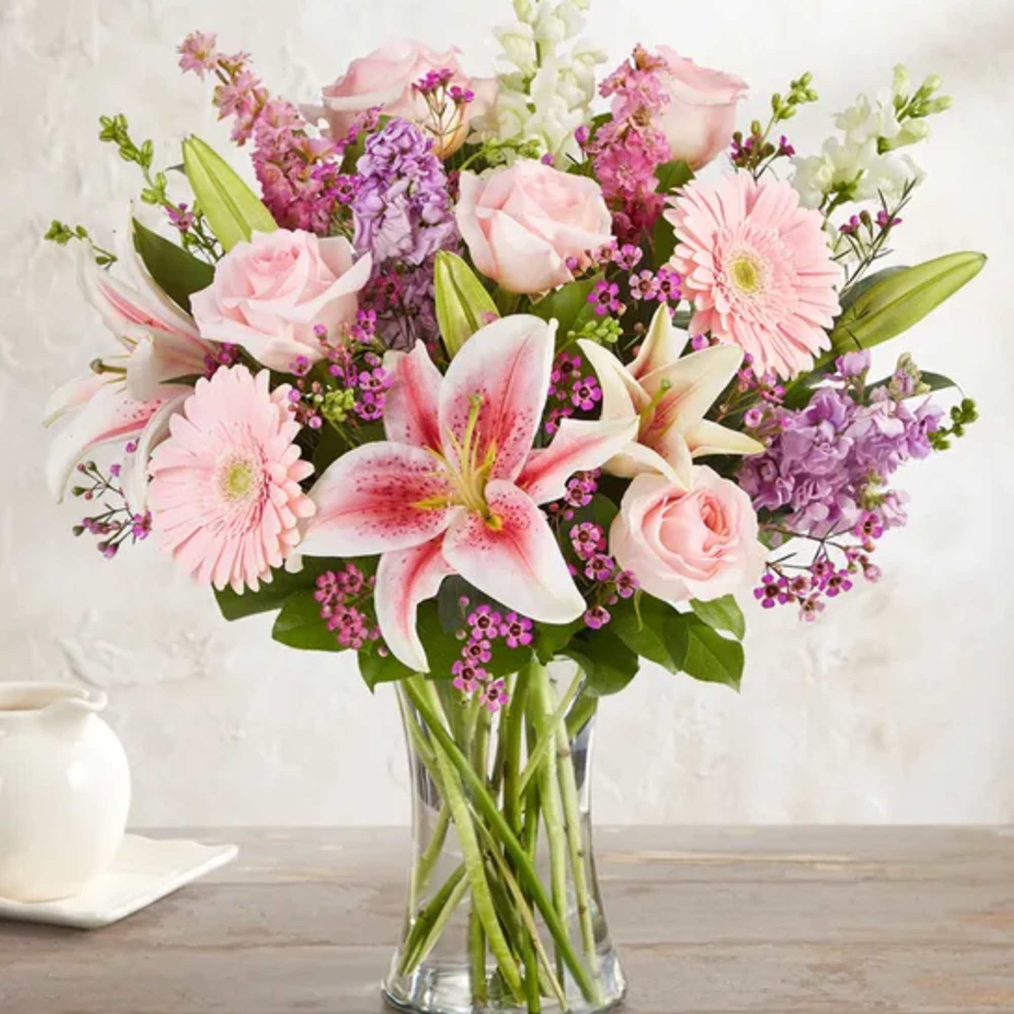 Pink roses, lilies, and gerbera daisies in a clear glass vase