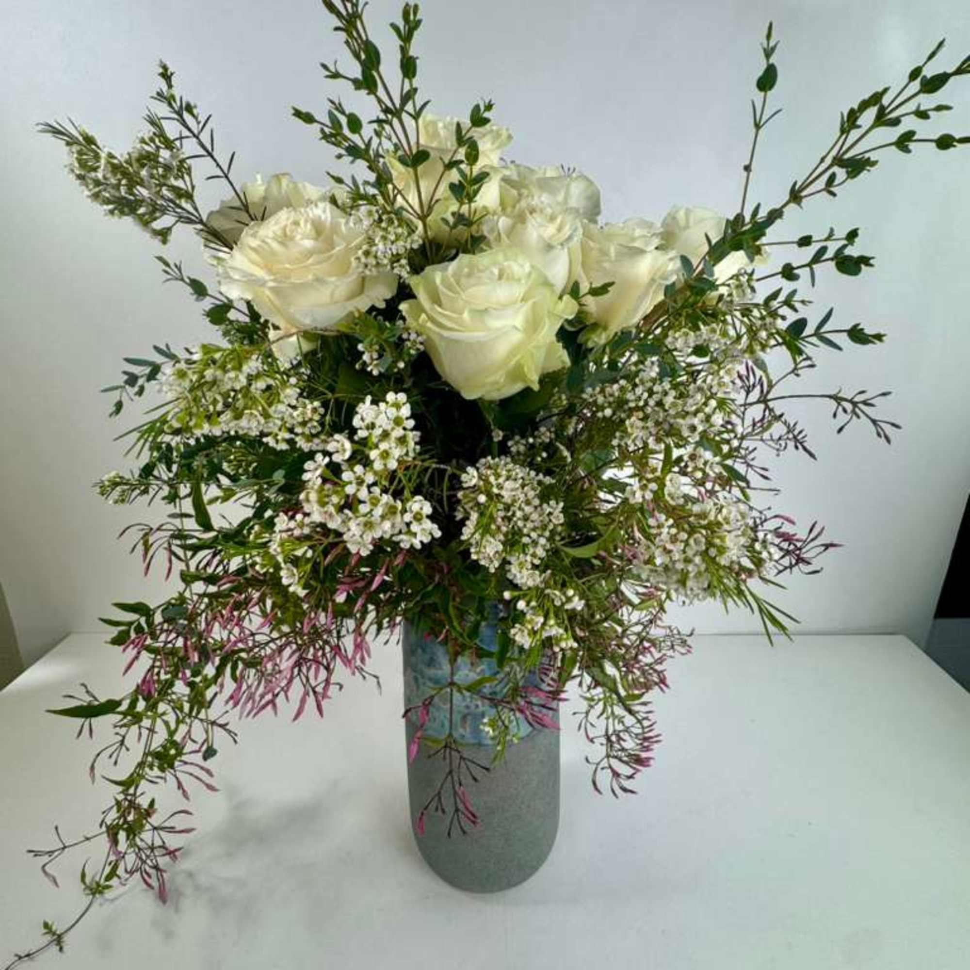 White roses in a gray vase with airy filler flowers and branching greenery