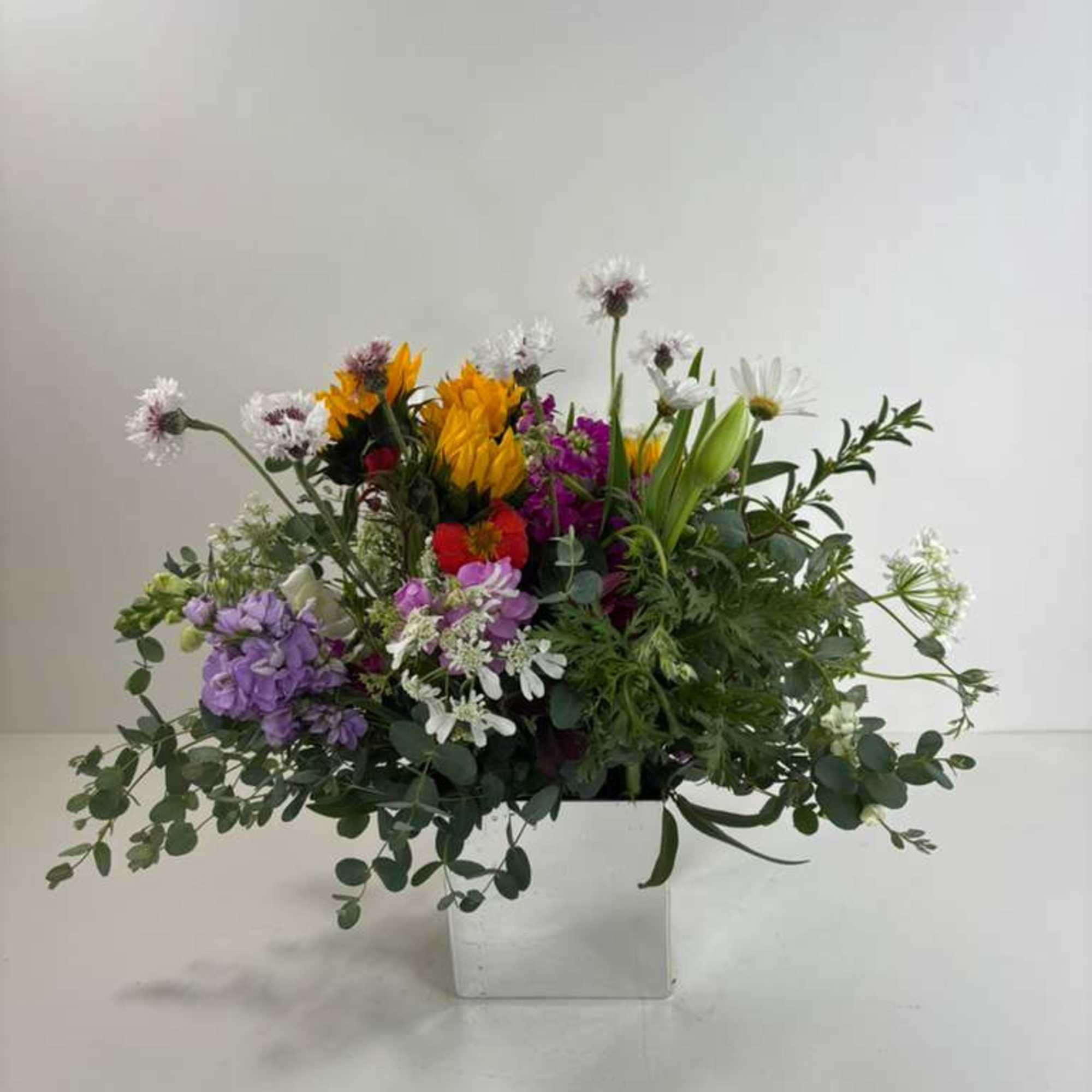 Mixed bouquet in a white square vase with purple, yellow, red, and white flowers