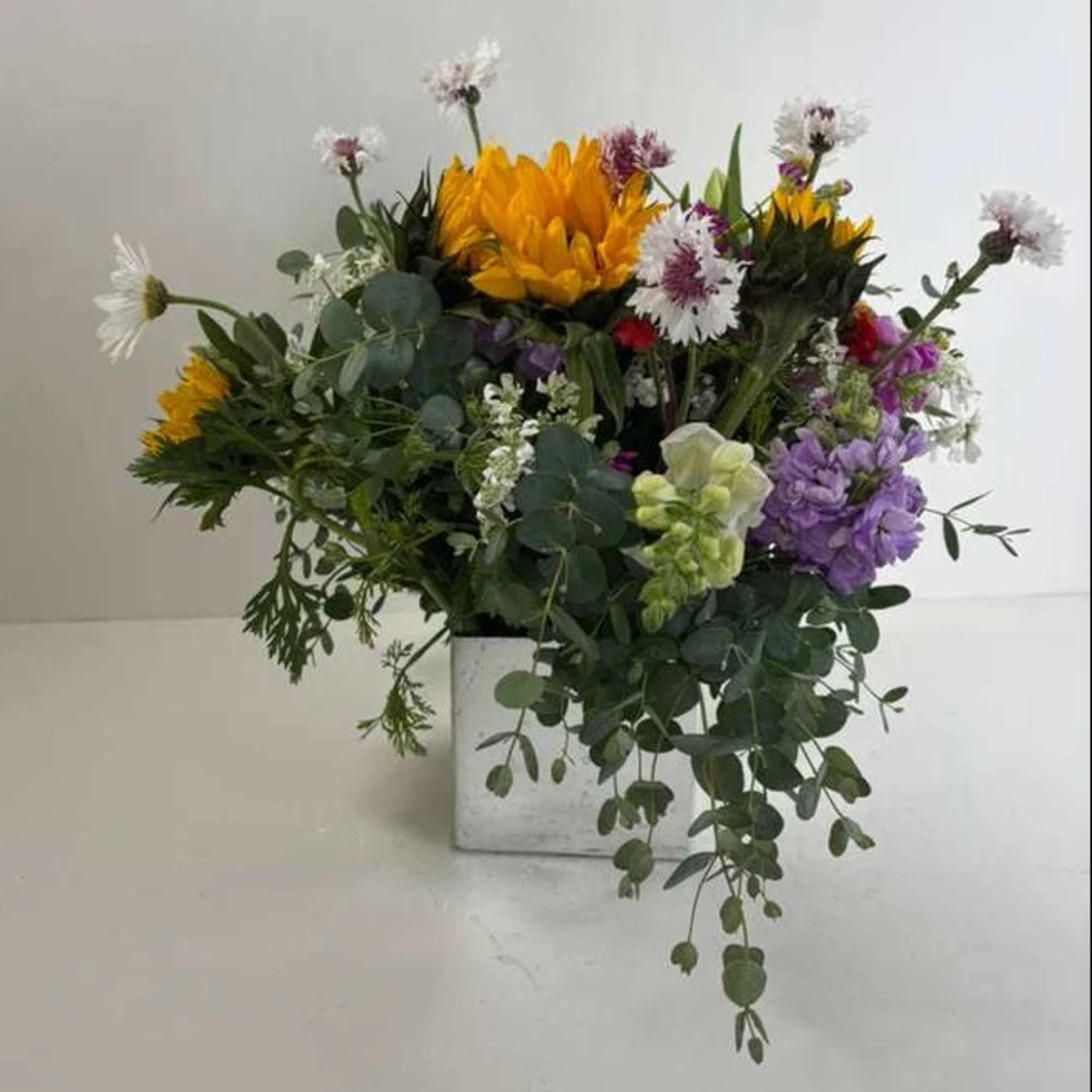 Mixed bouquet with yellow, purple, and white flowers in a white vase