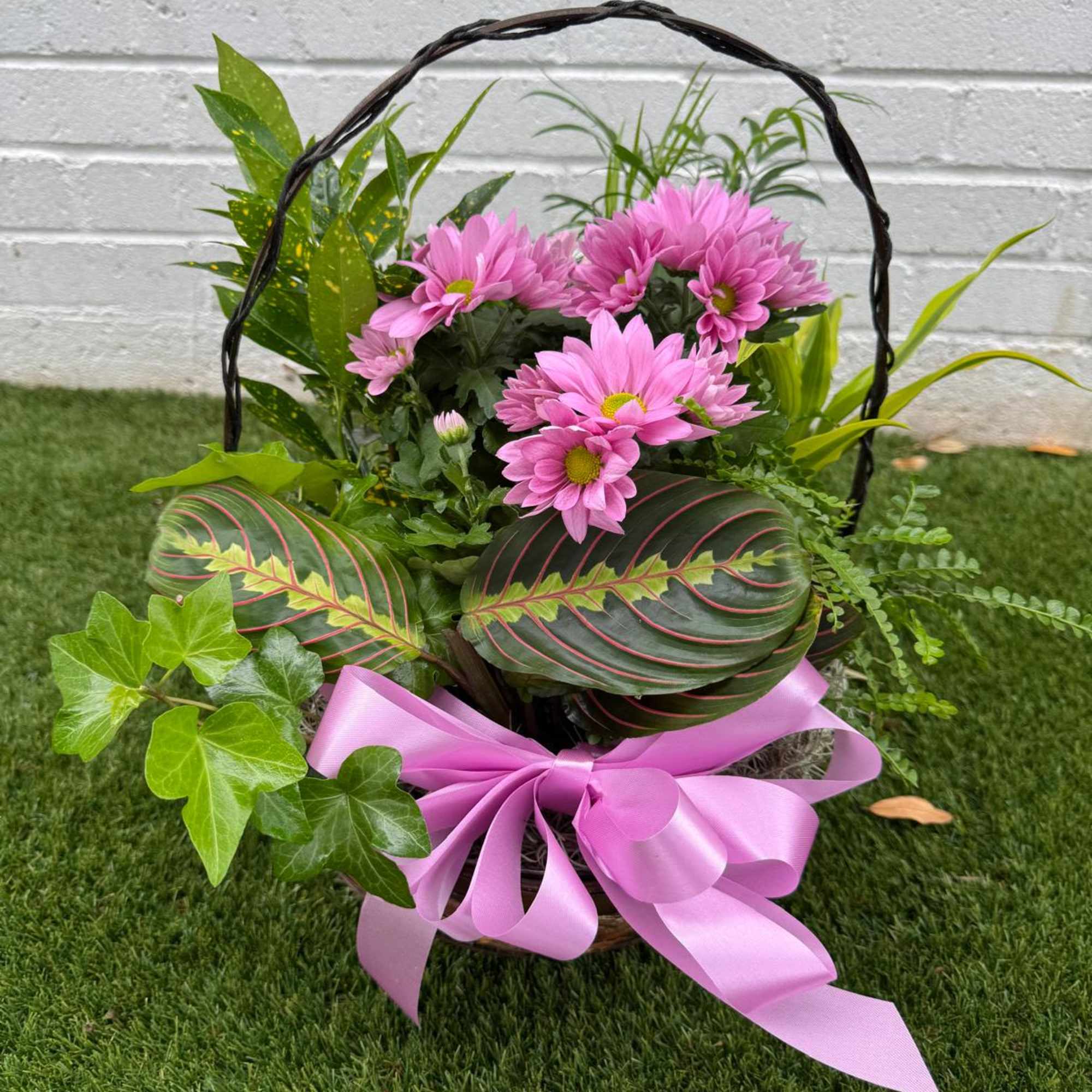 Basket of pink daisies with mixed greenery and a pink ribbon bow