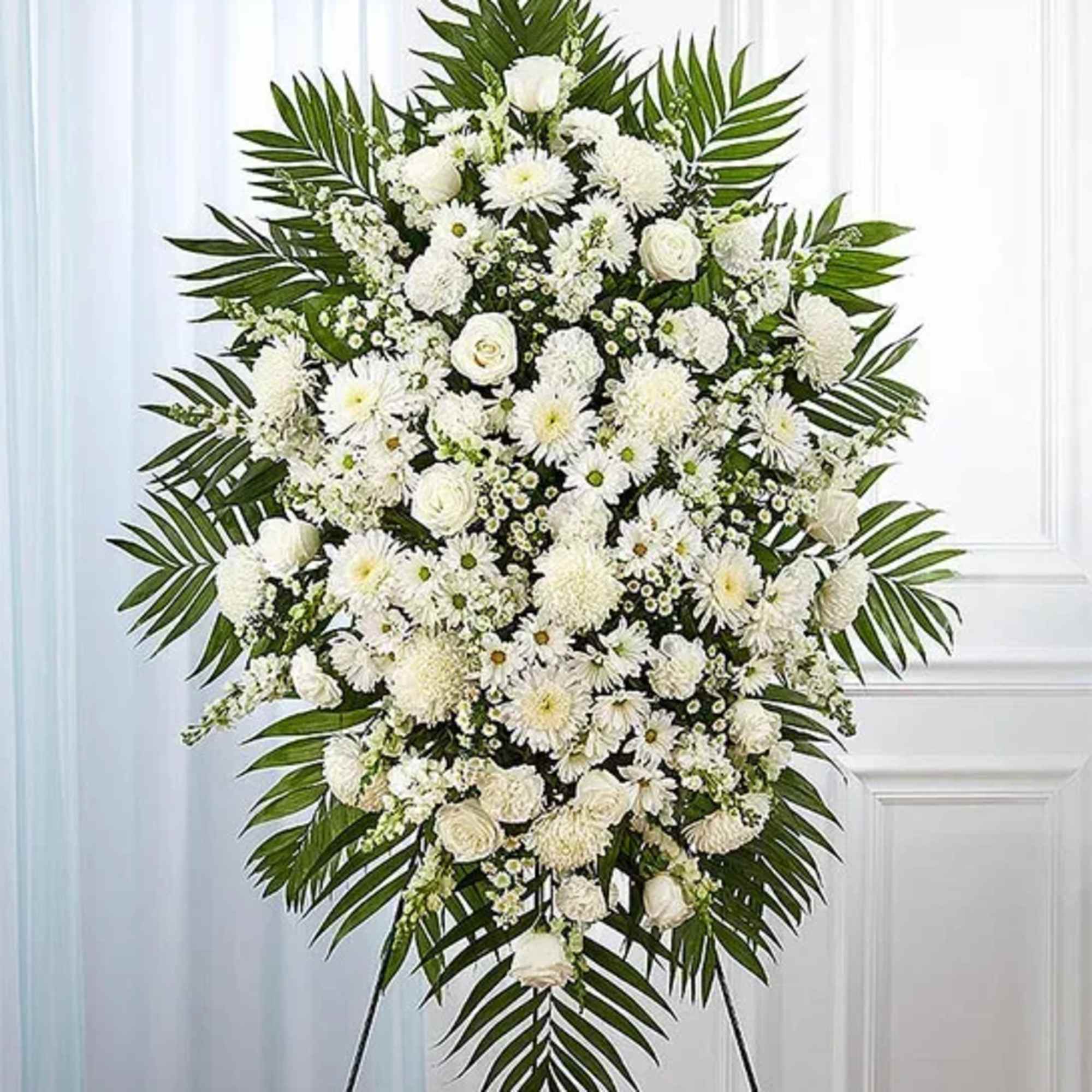 White funeral spray with mixed blooms and palm fronds on an easel