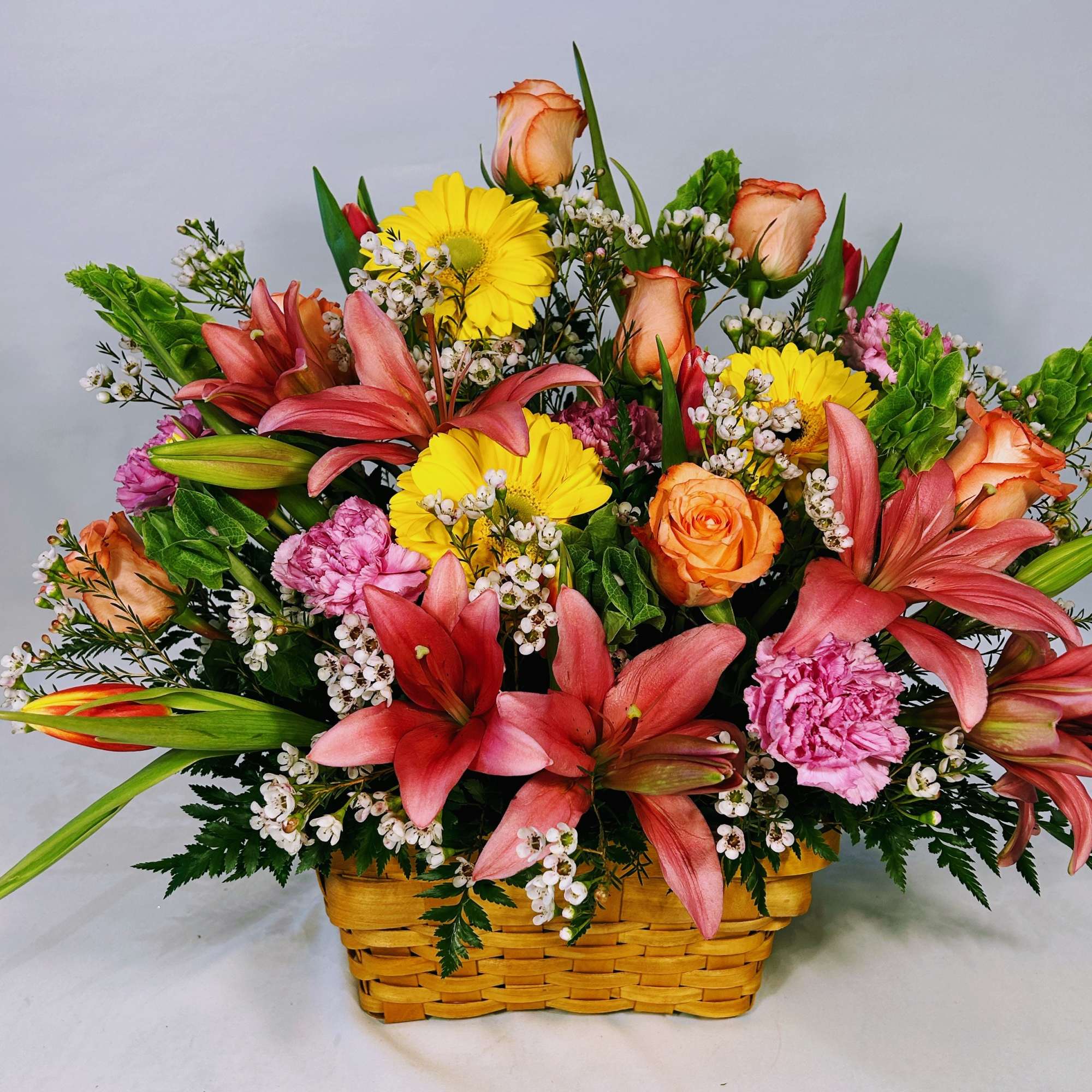 Colorful basket arrangement with pink lilies, yellow gerberas, orange roses, and pink carnations.