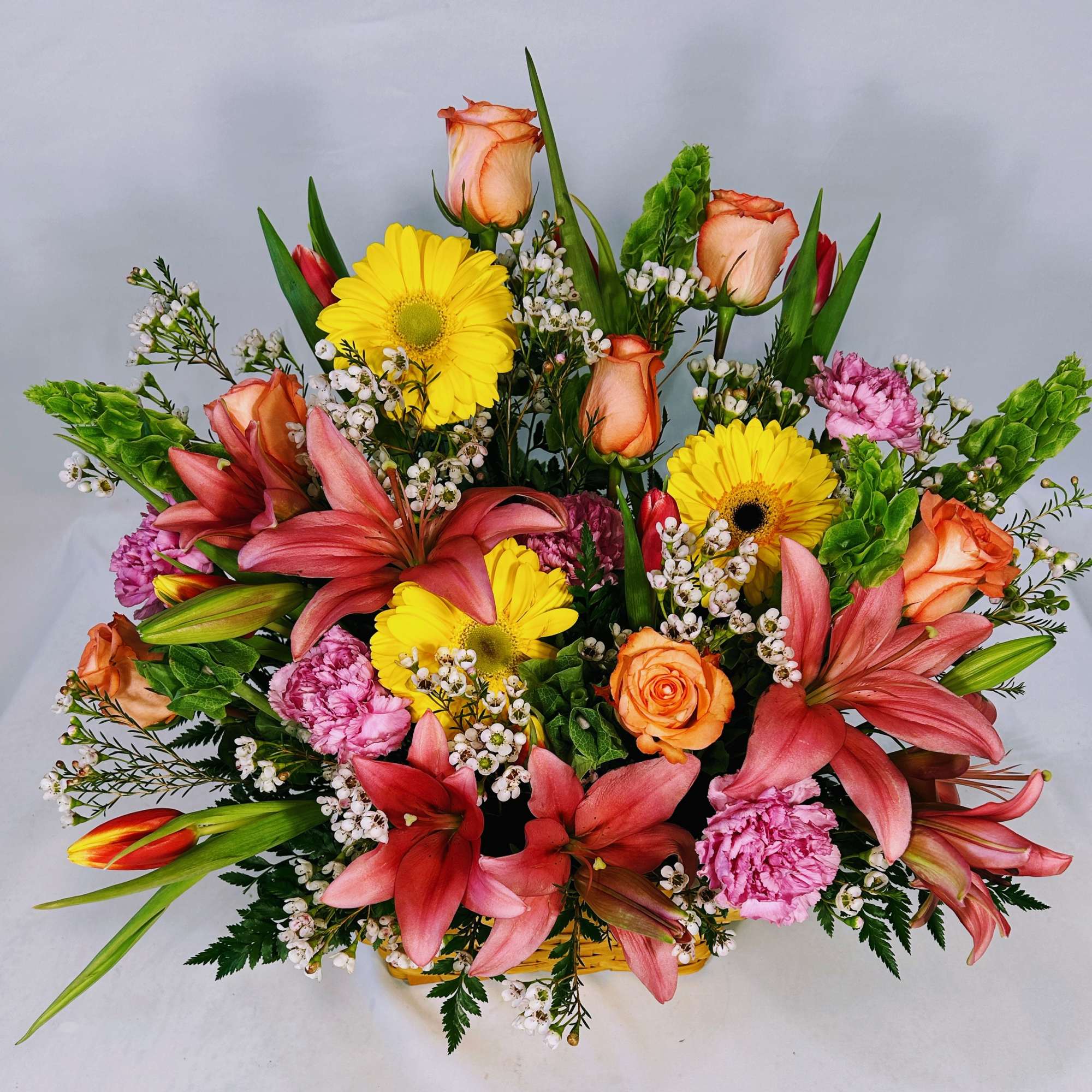 Bright mixed arrangement with pink lilies, yellow gerbera daisies, orange roses and pink carnations in a low basket
