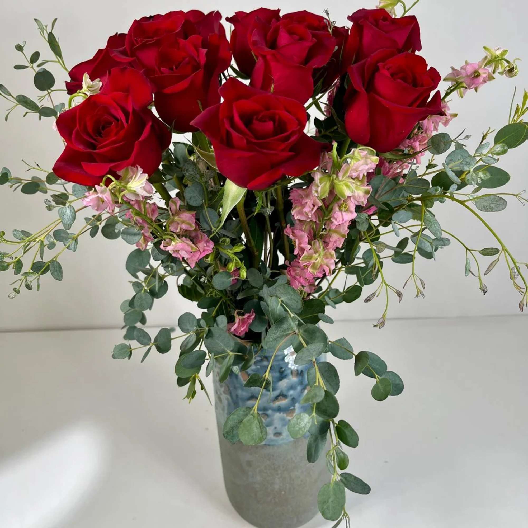 Red roses in a blue-gray vase with pink filler flowers and eucalyptus