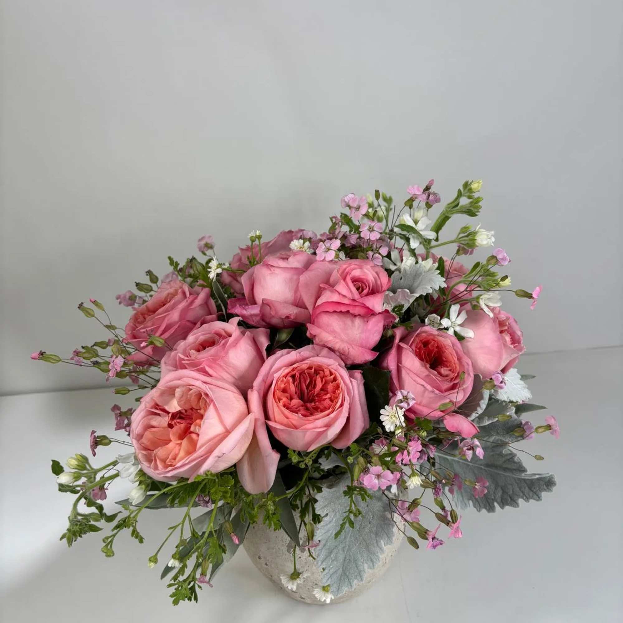 Pink rose bouquet in a white vase with small white and pink filler flowers