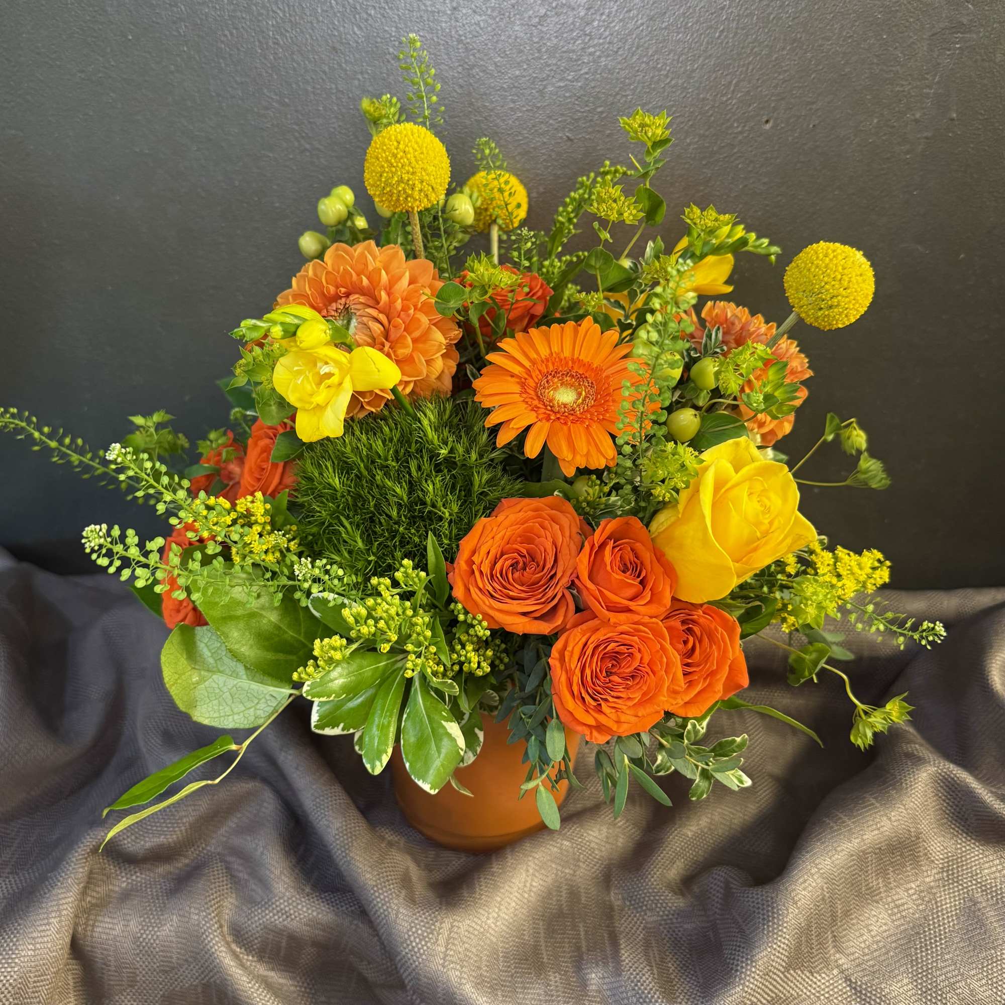 Orange and yellow mixed flower arrangement in a round vase