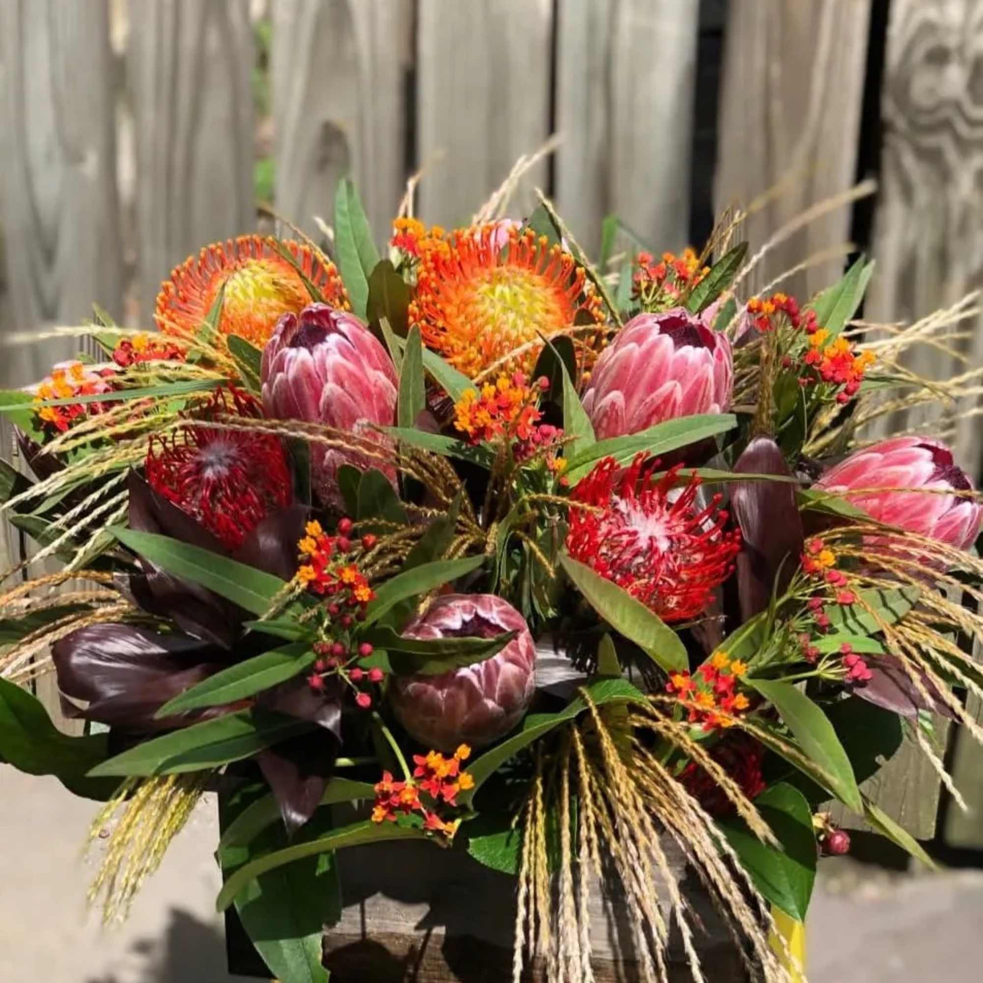 Bouquet of pink and orange protea with mixed greenery in a container